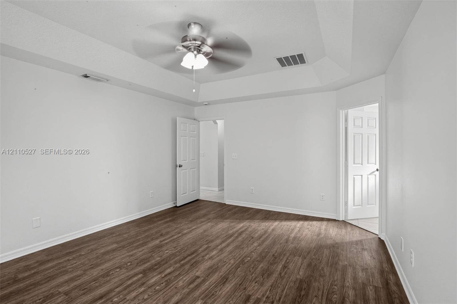 5509 NW Commodore Terrace, Port St Lucie, FL 34983 Tray ceiling featuring a central brushed-nickel ceiling fan with integrated lighting and wood-finish flooring