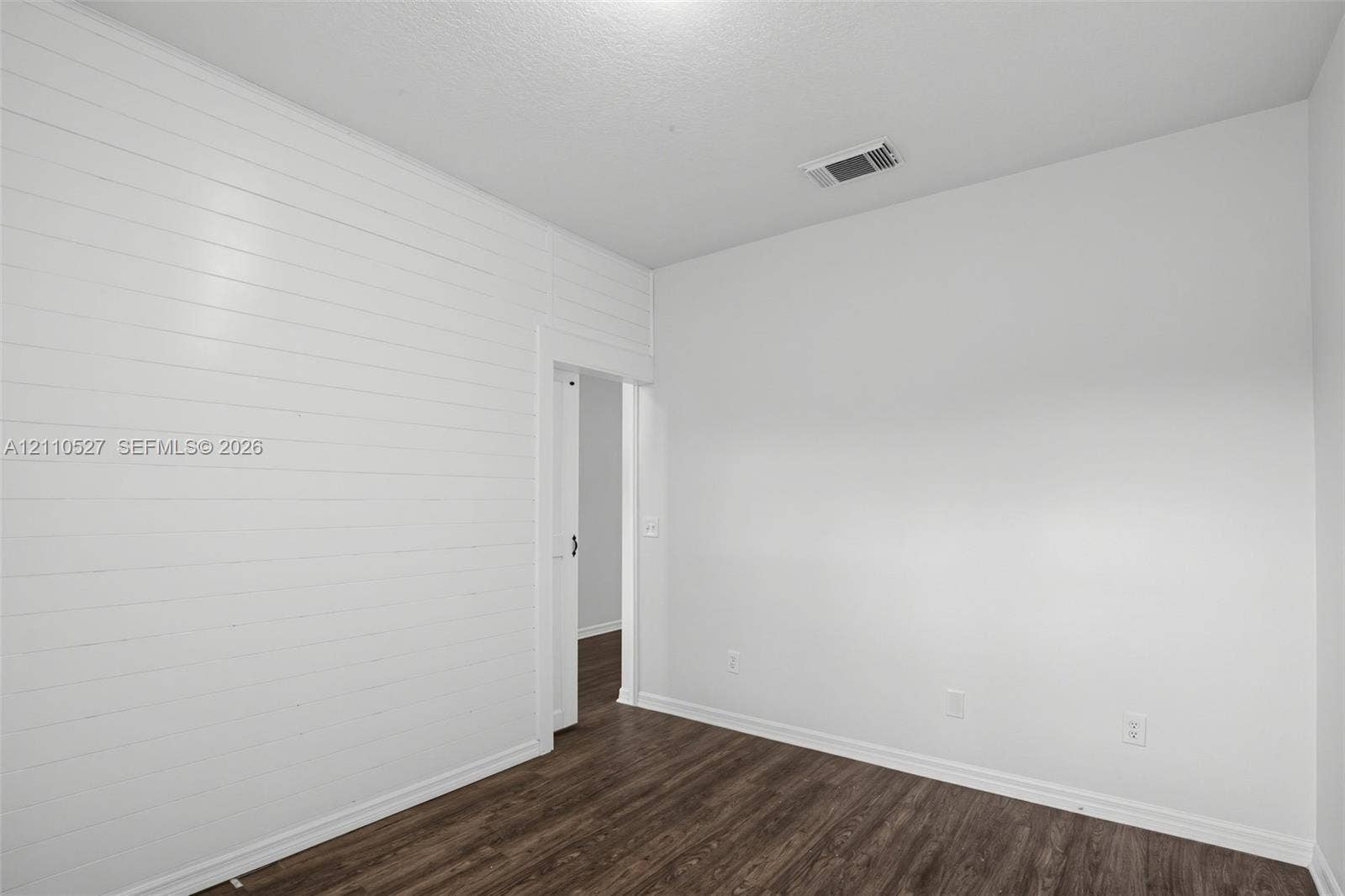 5509 NW Commodore Terrace, Port St Lucie, FL 34983 Room featuring horizontal shiplap wall paneling, dark wood-finish flooring, and a door opening