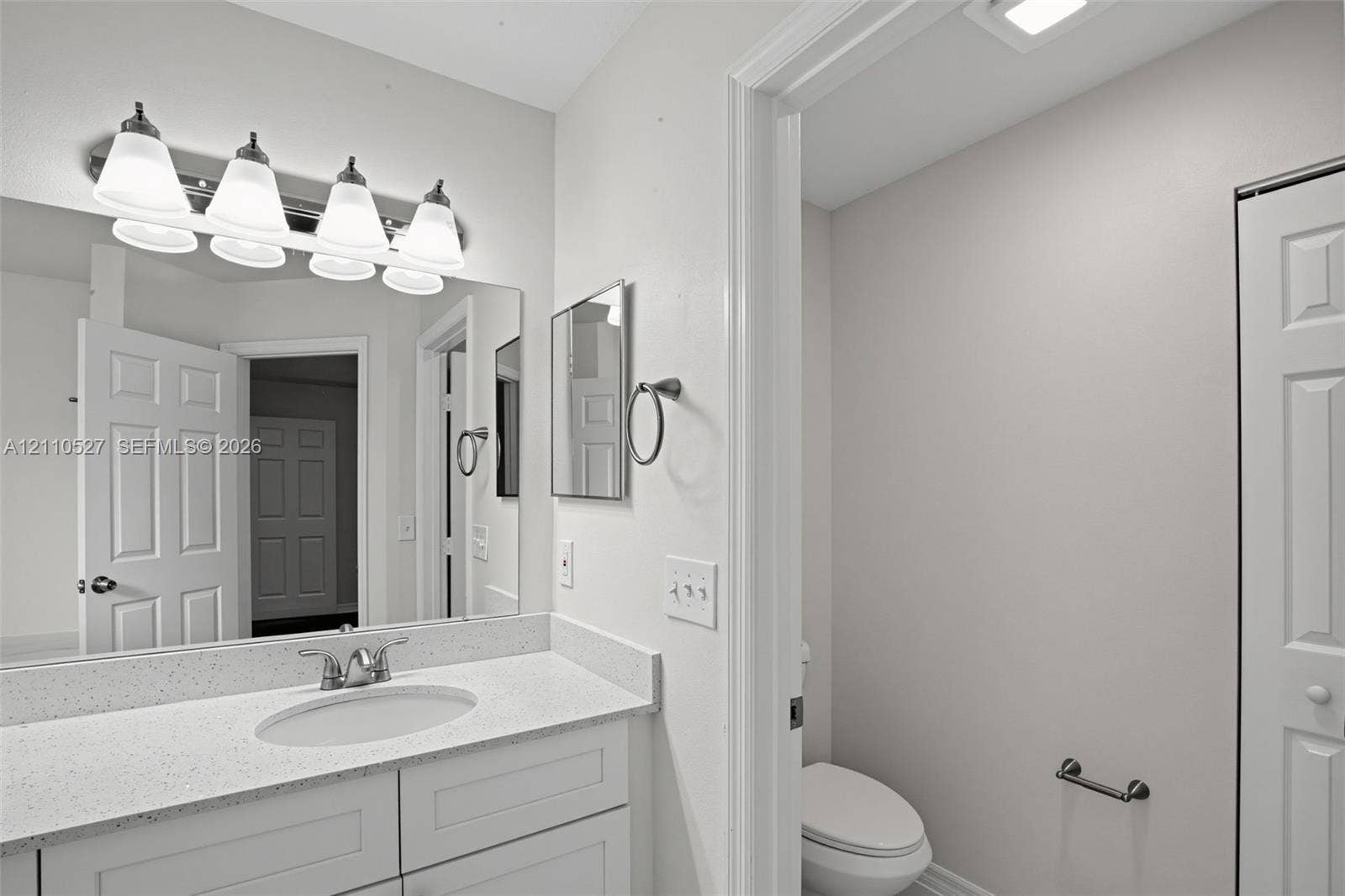5509 NW Commodore Terrace, Port St Lucie, FL 34983 Bathroom vanity featuring an integrated oval sink, stone-composite countertop, shaker-style cabinetry, a wall-to-wall mirror, and a four-light fixture