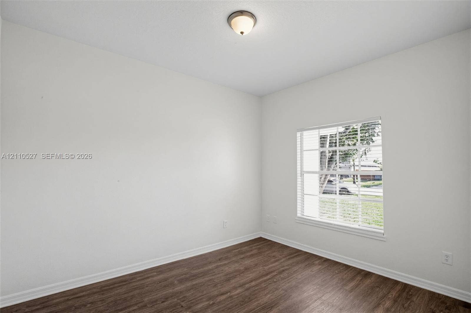 5509 NW Commodore Terrace, Port St Lucie, FL 34983 Room featuring neutral-toned walls, wood-finish flooring, a multi-pane window with integrated blinds, and a dome-style flush-mount ceiling light