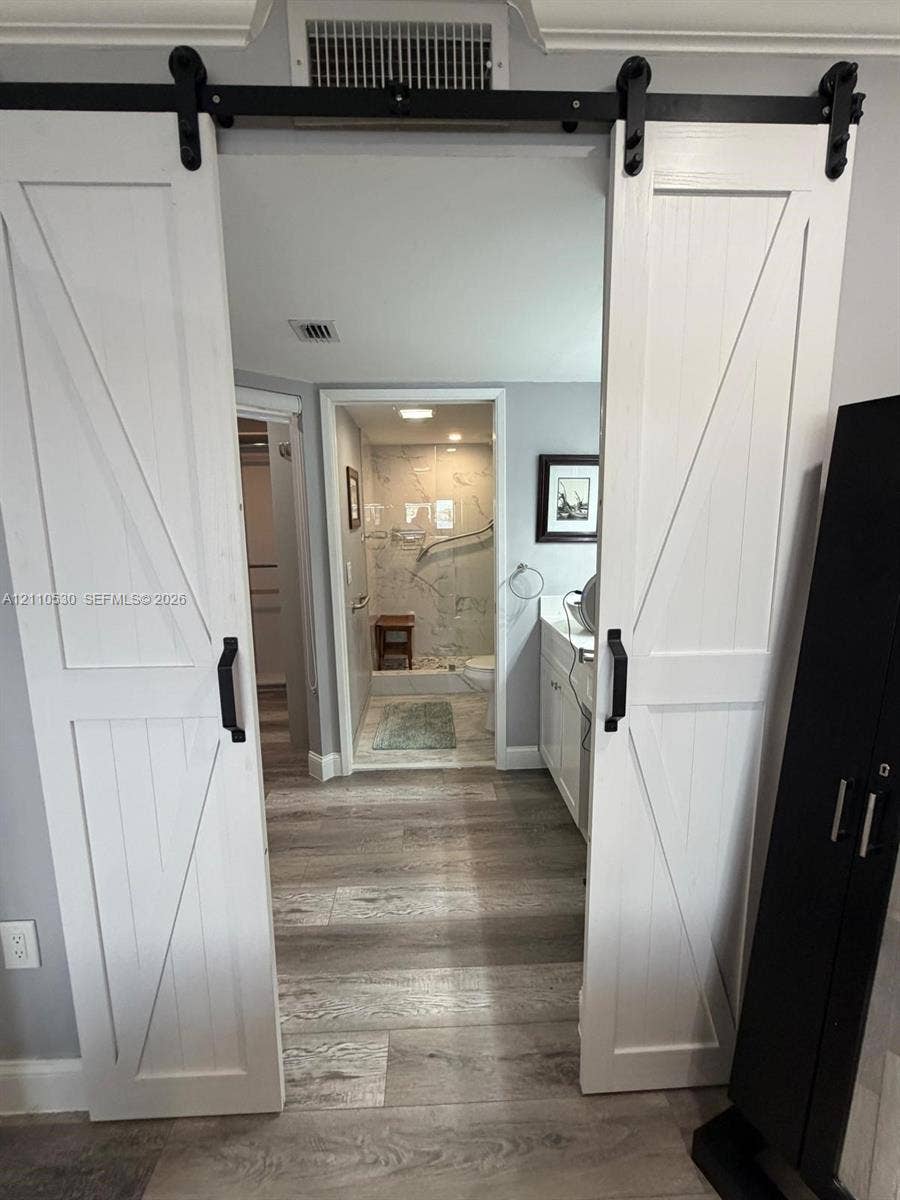 13255 SW 16th Court, #K112, Pembroke Pines, FL 33027 White barn-style sliding doors with black hardware, wood-finish flooring, white cabinetry, and shower enclosure with wall-mounted grab bars