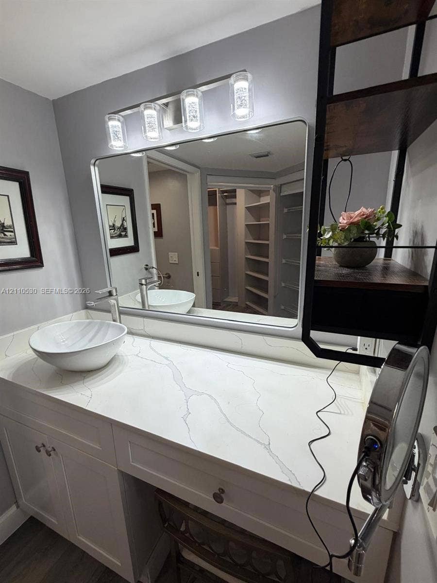 13255 SW 16th Court, #K112, Pembroke Pines, FL 33027 White vanity with a stone-finish countertop, round vessel sink, chrome faucet, rectangular mirror, and a four-light fixture
