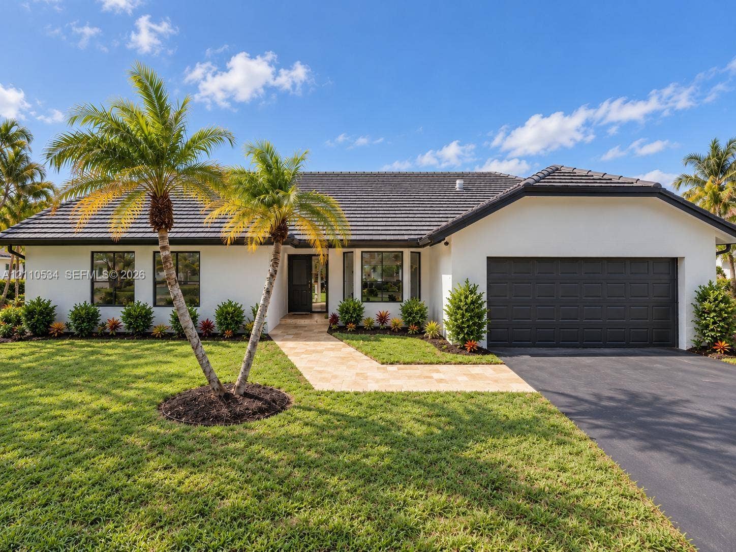 Single-story exterior featuring white stucco siding, a charcoal tile roof, a multi-paneled garage door, and a stone-paver walkway