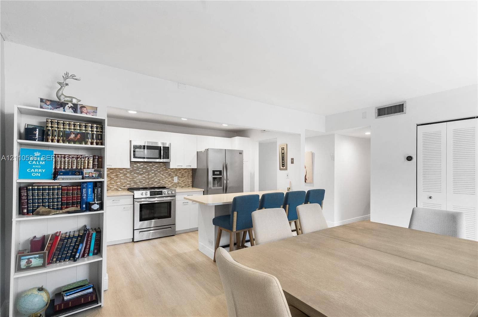 Kitchen featuring white cabinetry, stainless steel appliances, a center island with counter seating, and a decorative tile backsplash, complemented by wood-finish flooring