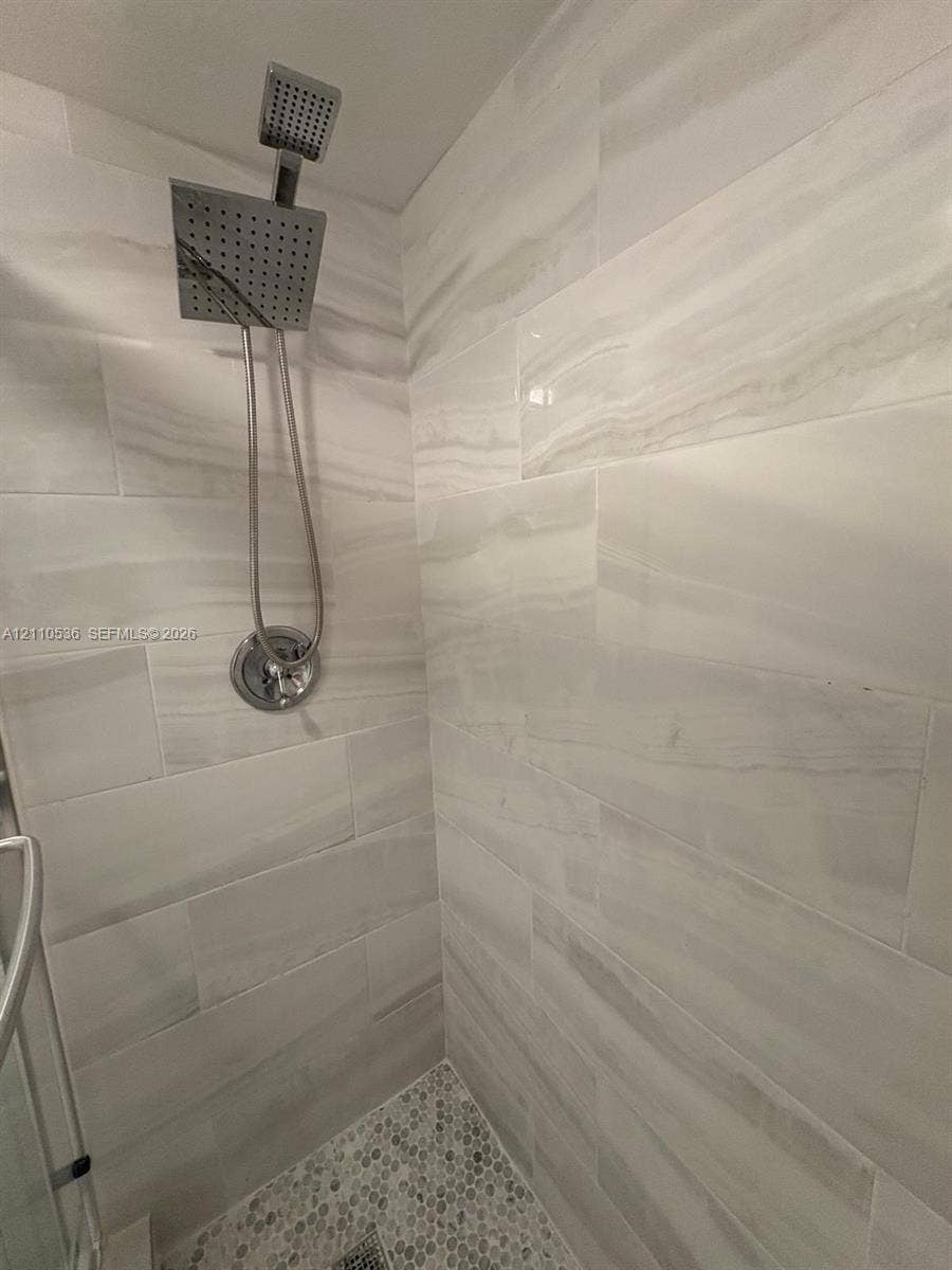 Shower stall featuring large-format stone-patterned wall tile, pebble-texture floor tile, and a polished chrome square rainfall showerhead with a handheld sprayer