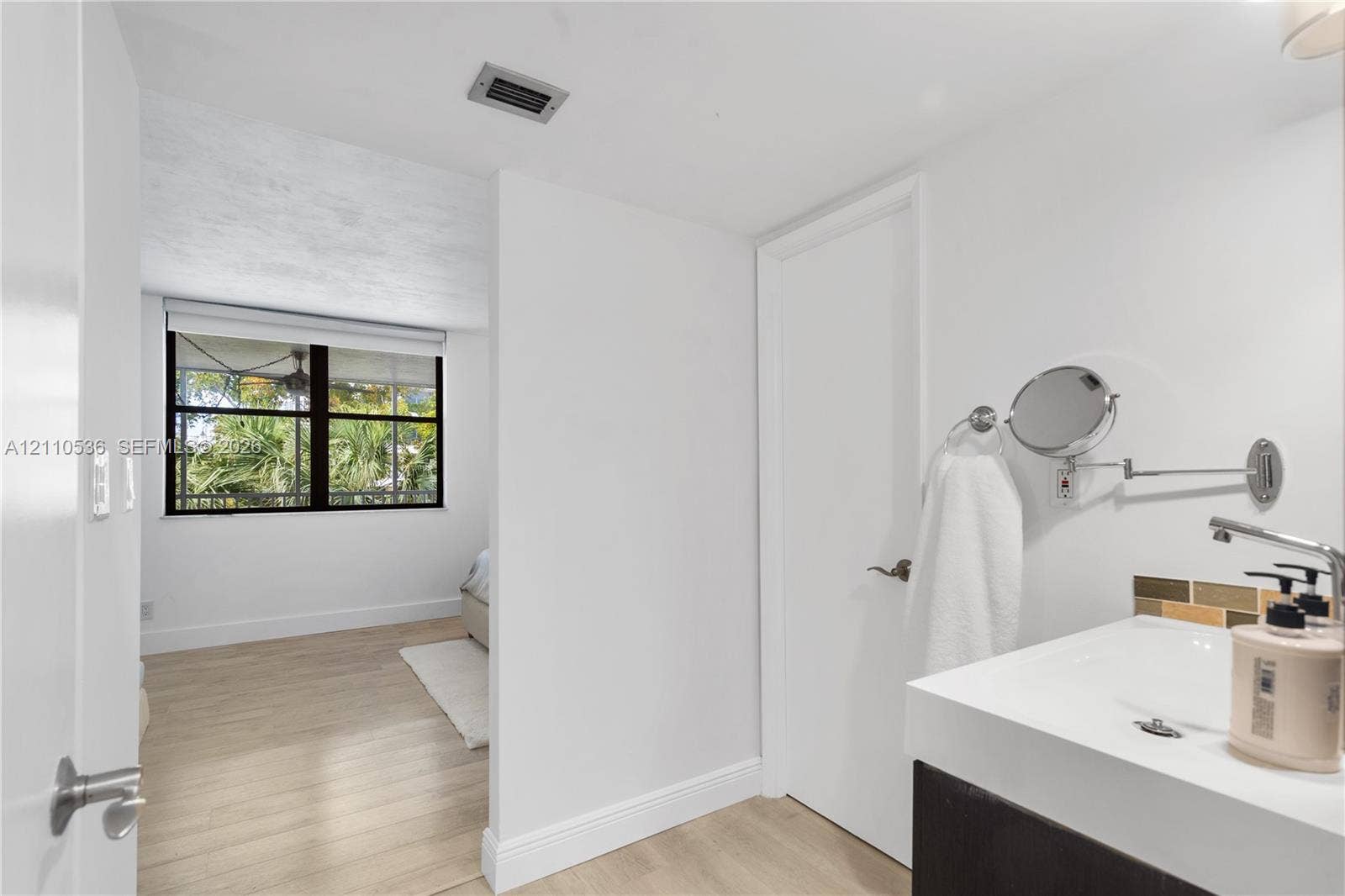 Bathroom vanity with a white rectangular basin and dark cabinetry, paired with a wall-mounted extendable vanity mirror and light-toned wood-finish flooring