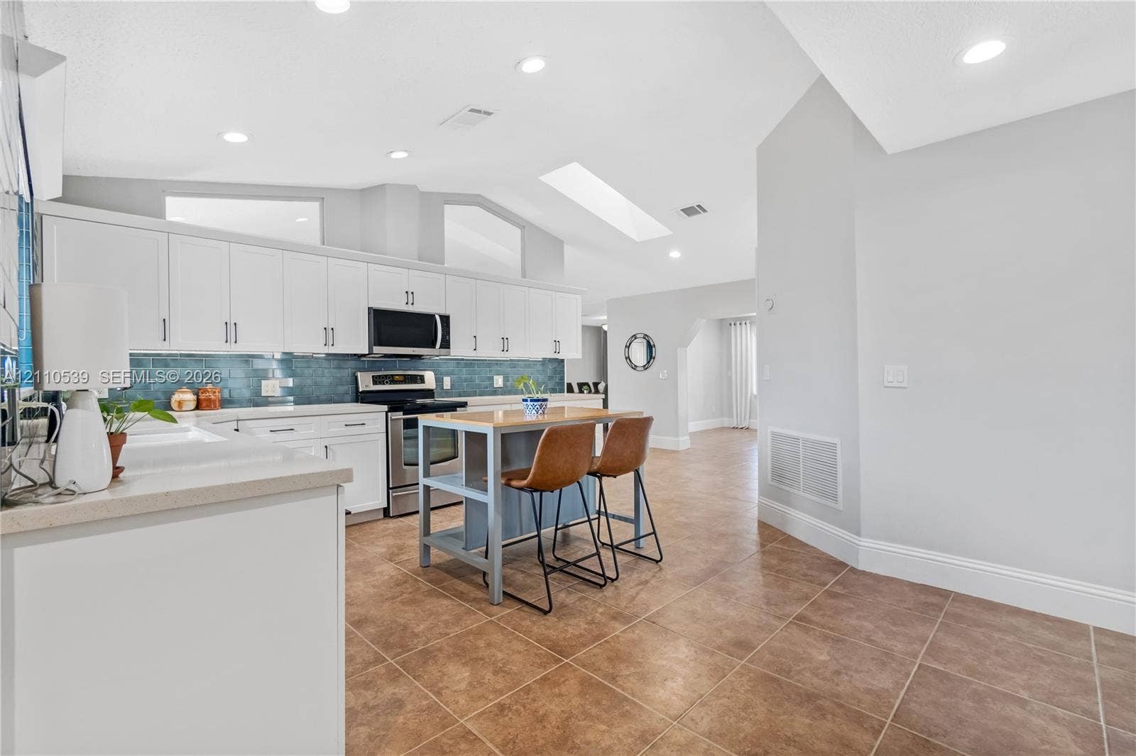 Kitchen featuring white cabinetry, stainless steel appliances, blue tile backsplash, a central island, and a skylight