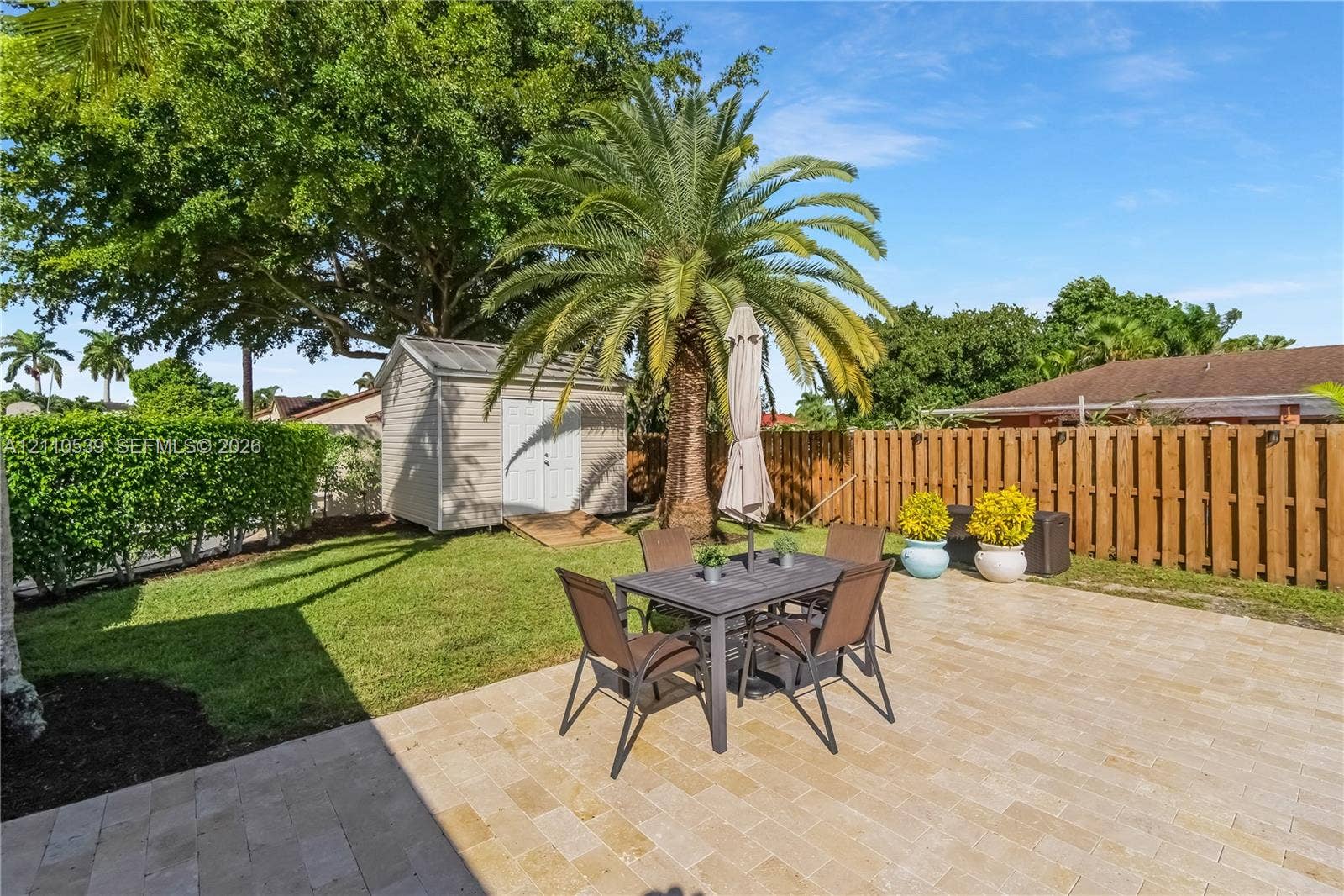 Private backyard featuring a paved stone patio, mature palm tree, manicured lawn, wood privacy fencing, and a detached storage shed