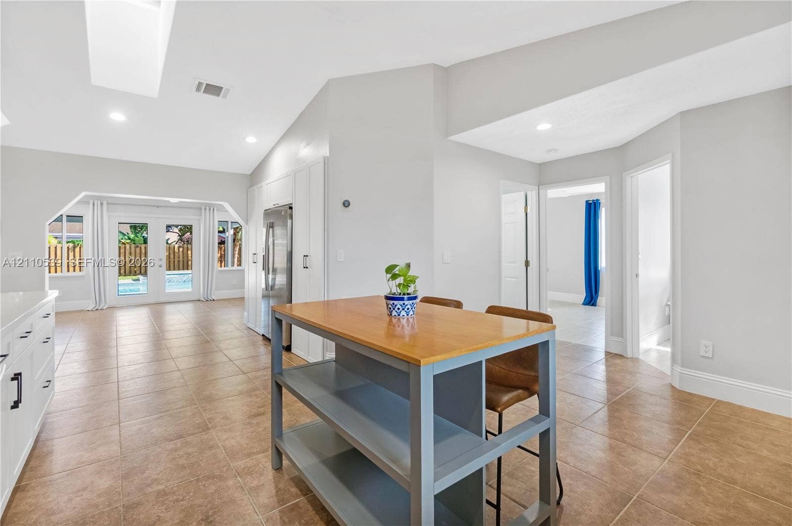 Vaulted ceiling with recessed lighting, neutral tile flooring, white cabinetry, and glass paneled double doors