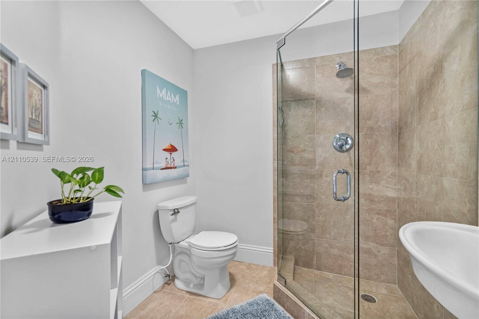 Bathroom featuring a corner glass-enclosed shower with full-height stone-finish tile surround, chrome shower hardware, and a pedestal sink