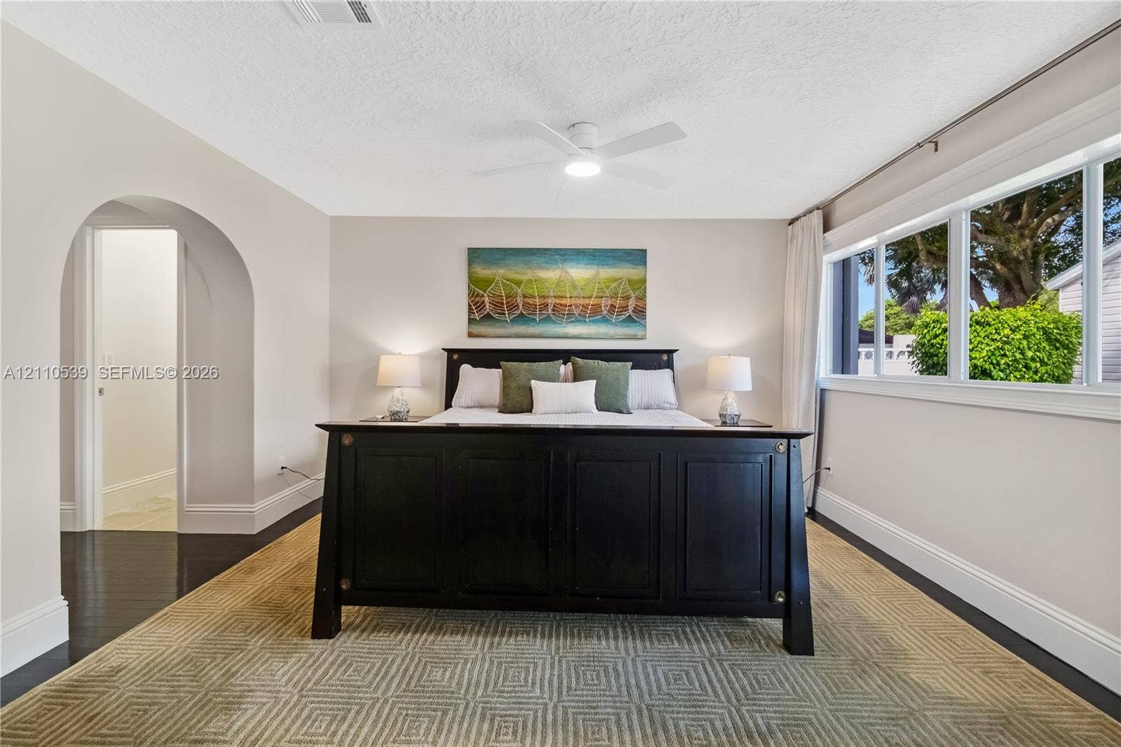 Neutral-toned walls with an arched entryway, wood-finish flooring, a ceiling-mounted light fixture with fan, and expansive horizontal windows