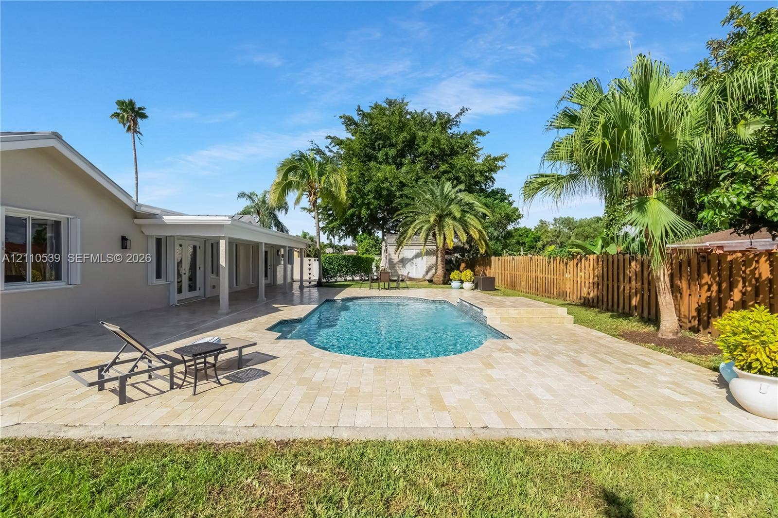 Backyard featuring a paver patio, in-ground swimming pool, covered outdoor living area, wood privacy fencing, and mature palm trees