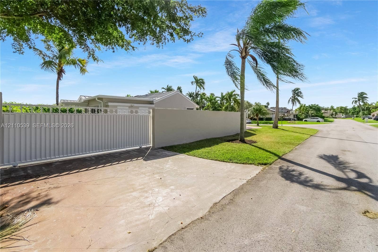 Private gated entrance featuring a solid concrete perimeter wall, metal sliding gate, and mature palm landscaping