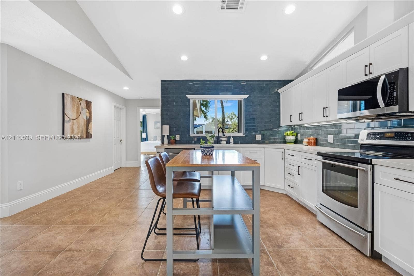 Kitchen featuring white cabinetry, blue tiled backsplash, stainless steel appliances, ceramic tile flooring, and vaulted ceilings with recessed lighting