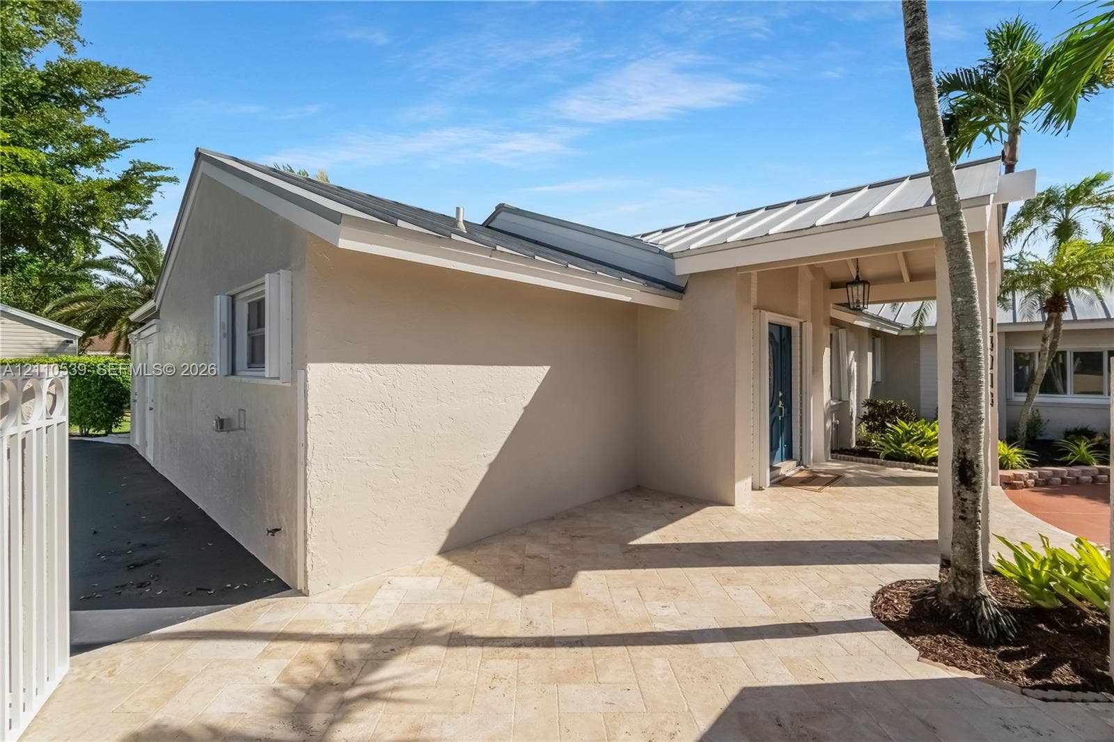 Stucco exterior featuring a metal roof, stone-paved entryway, and covered porch