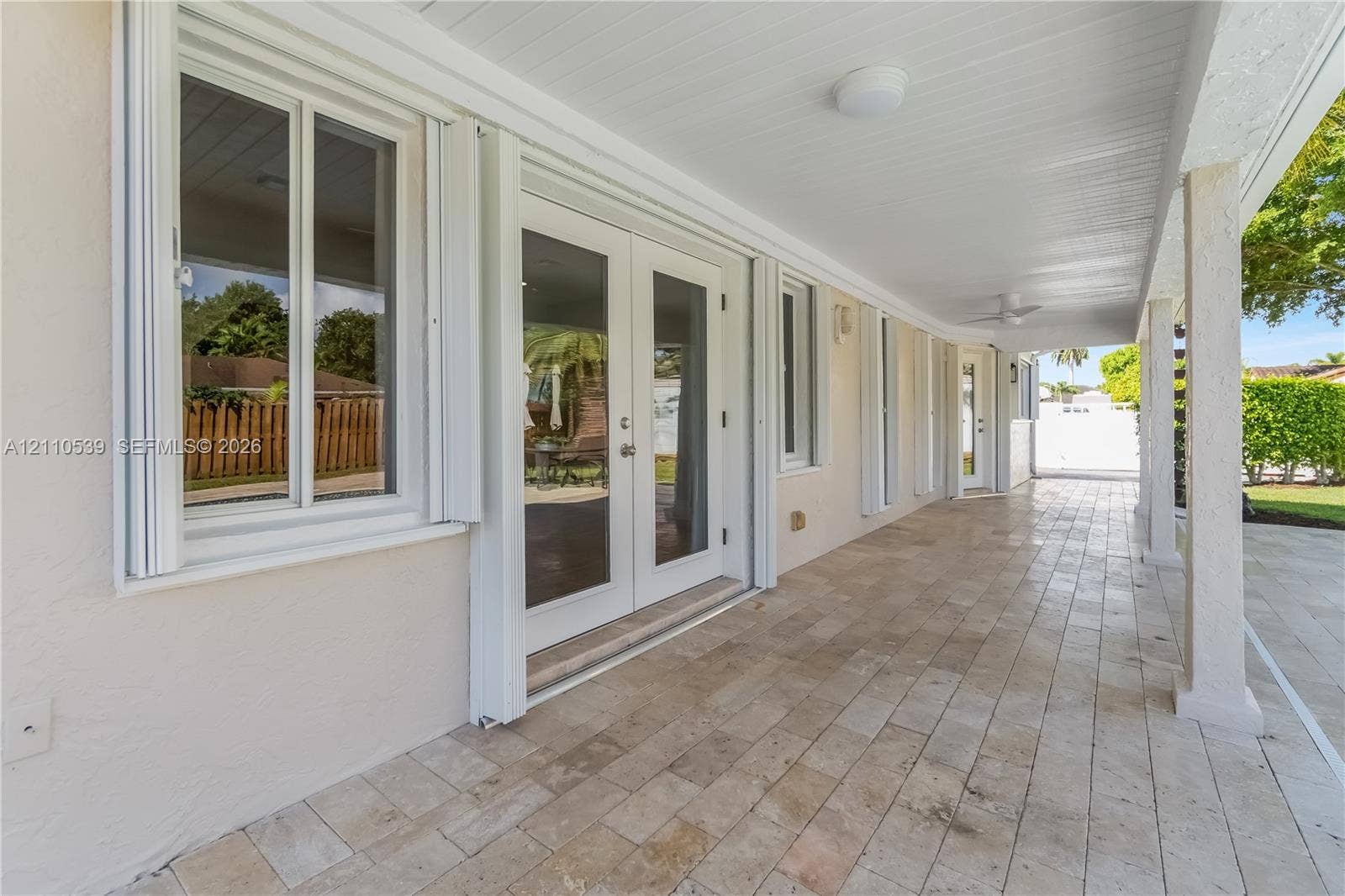 Covered patio featuring stone-tile flooring, glass-paned double doors, white-trimmed windows, and ceiling-mounted light fixtures