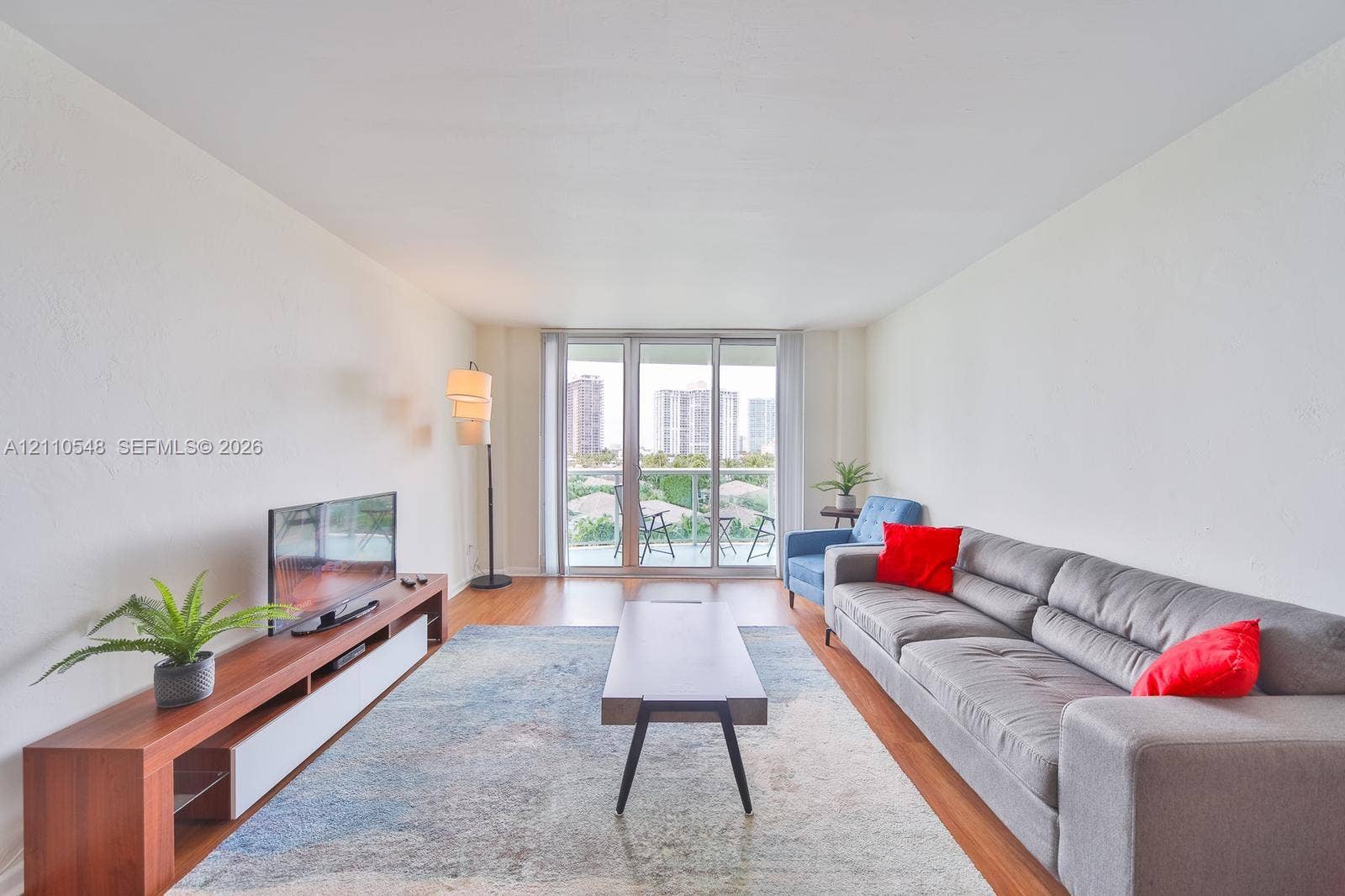 Living area featuring wood-finish flooring, white walls, and floor-to-ceiling glass sliding doors opening to a private balcony