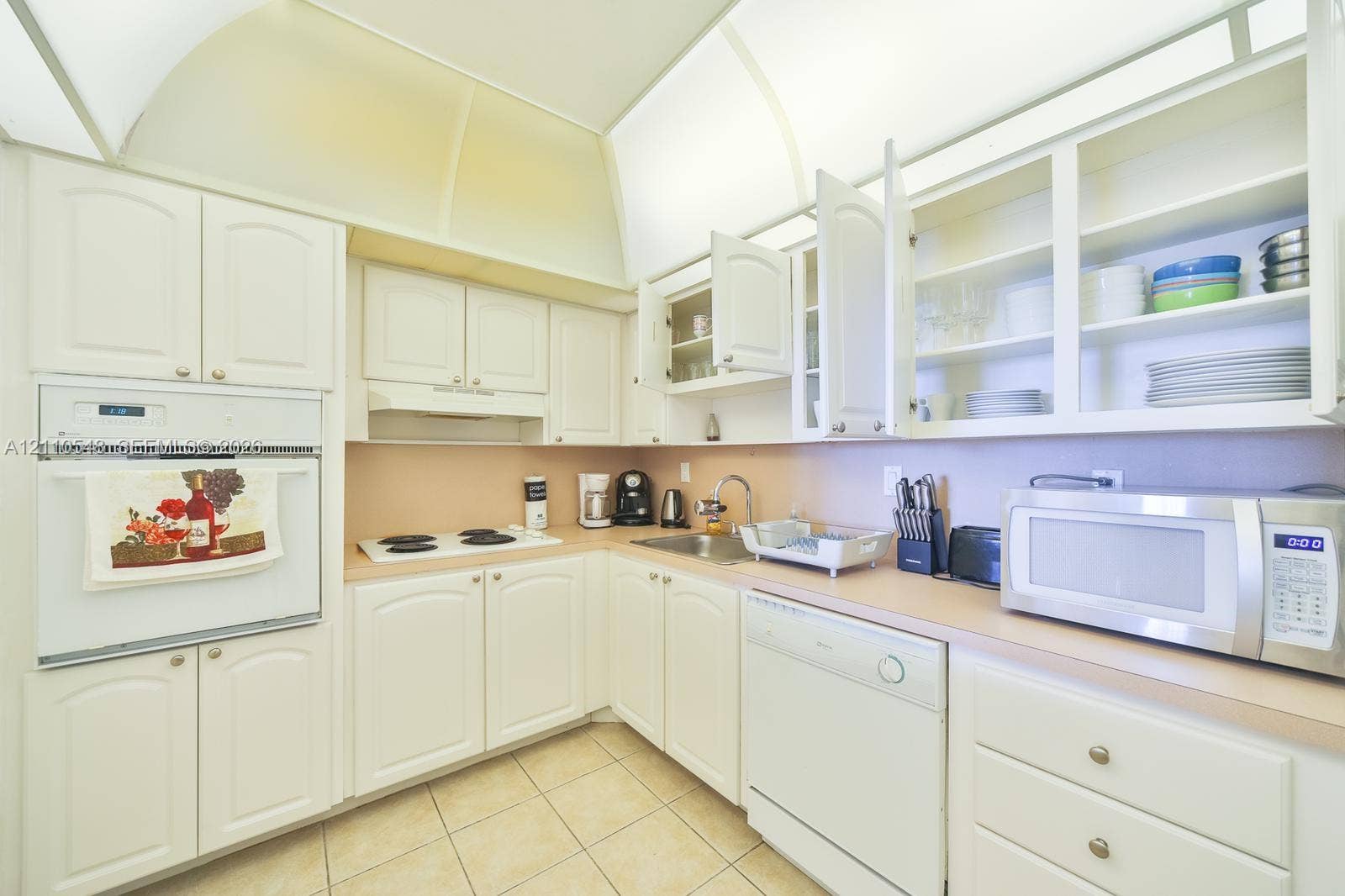Kitchen featuring white cabinetry with glass-front display uppers, integrated wall oven, solid-surface countertops, and ceramic tile flooring