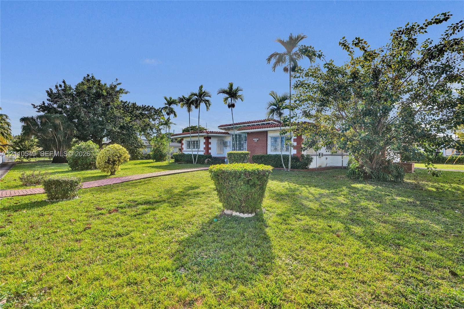 500 SW 39th Court, Miami, FL 33134 Single-story residence featuring a tile roof, brick exterior accents, multi-pane windows, and a paved walkway situated on a lot with mature palm trees