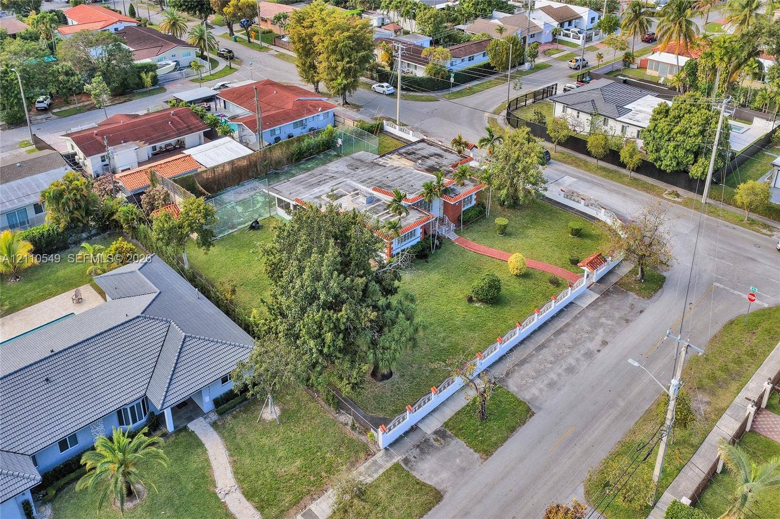 500 SW 39th Court, Miami, FL 33134 Corner lot residence featuring a fenced yard, private tennis court, mature trees, and a paved walkway