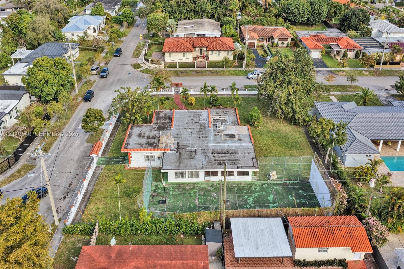 500 SW 39th Court, Miami, FL 33134 Aerial perspective of a corner lot property featuring a single-story residence, a private fenced-in sport court, expansive green space, and mature landscaping