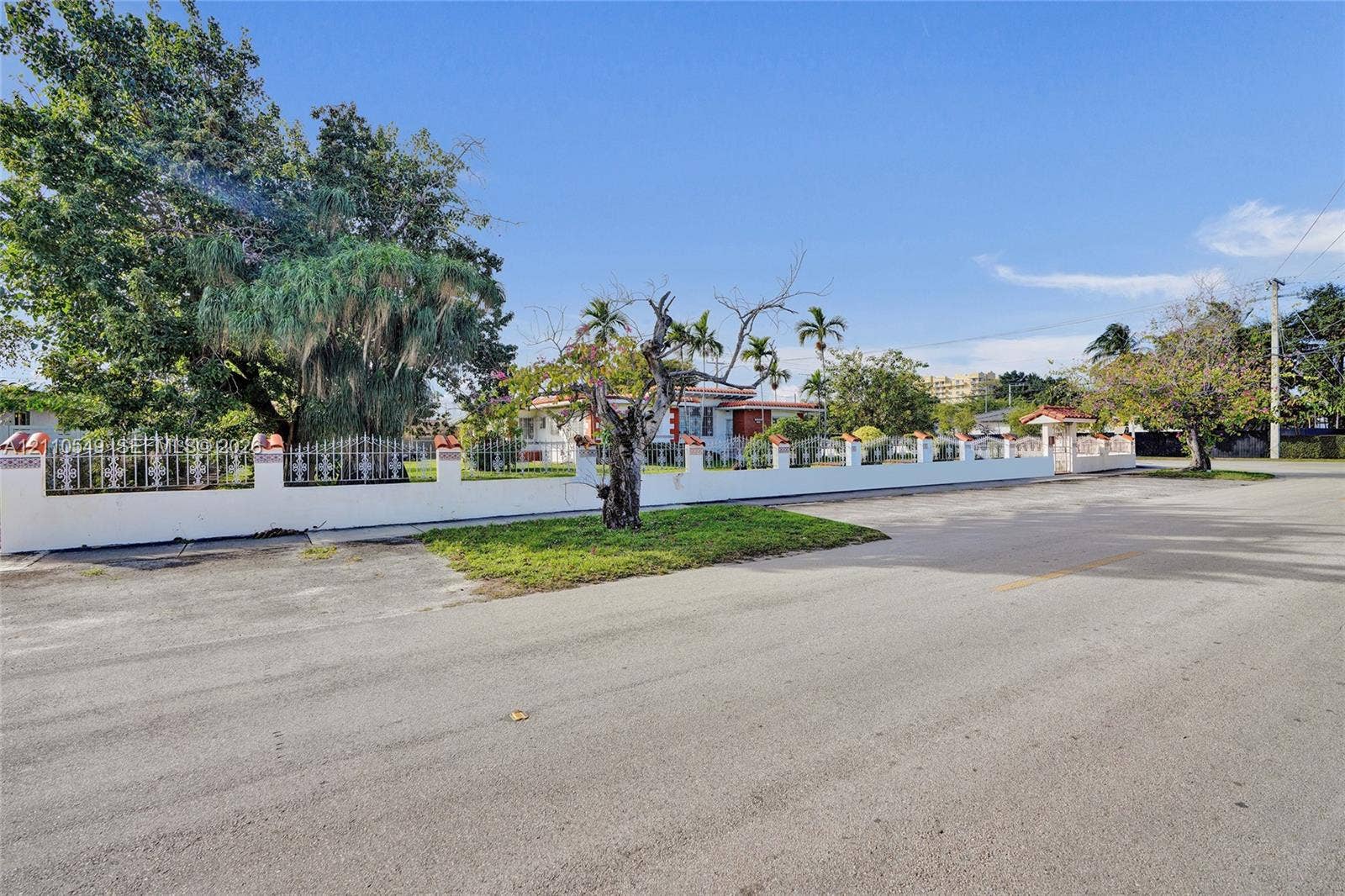 500 SW 39th Court, Miami, FL 33134 Property exterior featuring a white masonry perimeter wall with integrated metal decorative accents, a tiled column entryway, mature trees, and landscaping