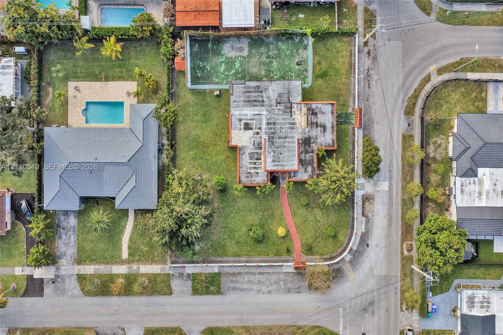 500 SW 39th Court, Miami, FL 33134 Aerial view of the property featuring a private fenced-in tennis court, expansive lawn, and paved walkway