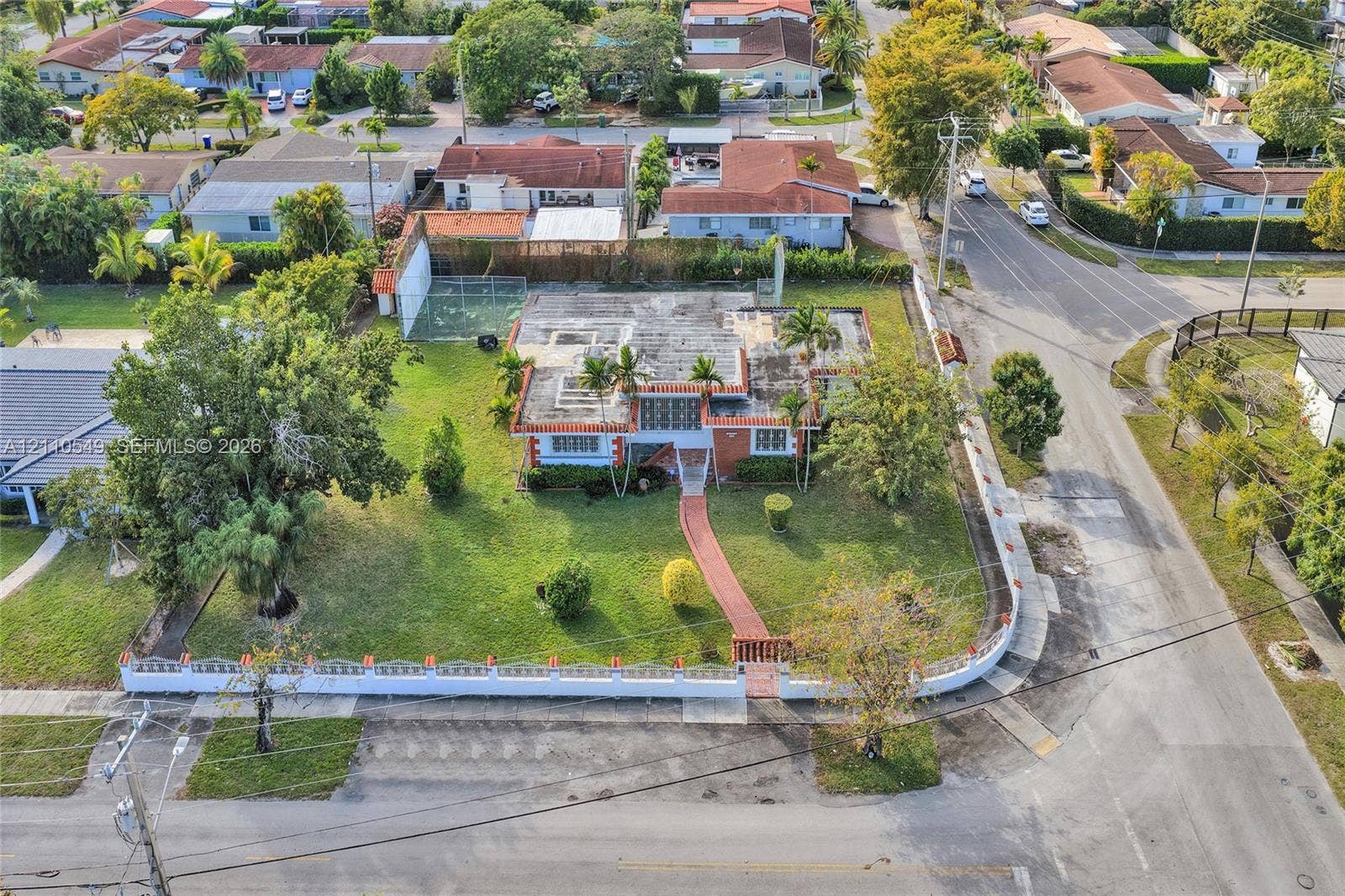 500 SW 39th Court, Miami, FL 33134 Corner lot property featuring a masonry perimeter wall, paved walkway, mature trees, and an enclosed hardscaped recreational area