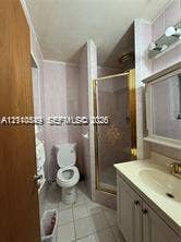 500 SW 39th Court, Miami, FL 33134 Bathroom featuring a vanity with integrated sink, brass-tone hardware, a wall-mounted medicine cabinet with integrated lighting, a stand-up shower enclosure with glass door, and tile flooring