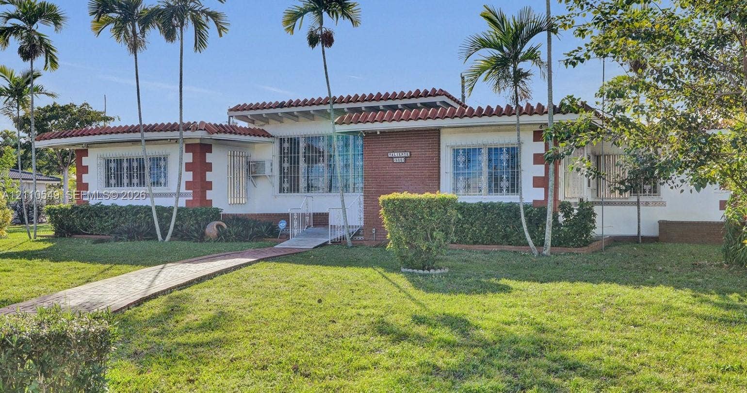 500 SW 39th Court, Miami, FL 33134 Single-story residence featuring a tile roof, brick masonry accents, white stucco exterior, and a paved walkway leading to the entryway