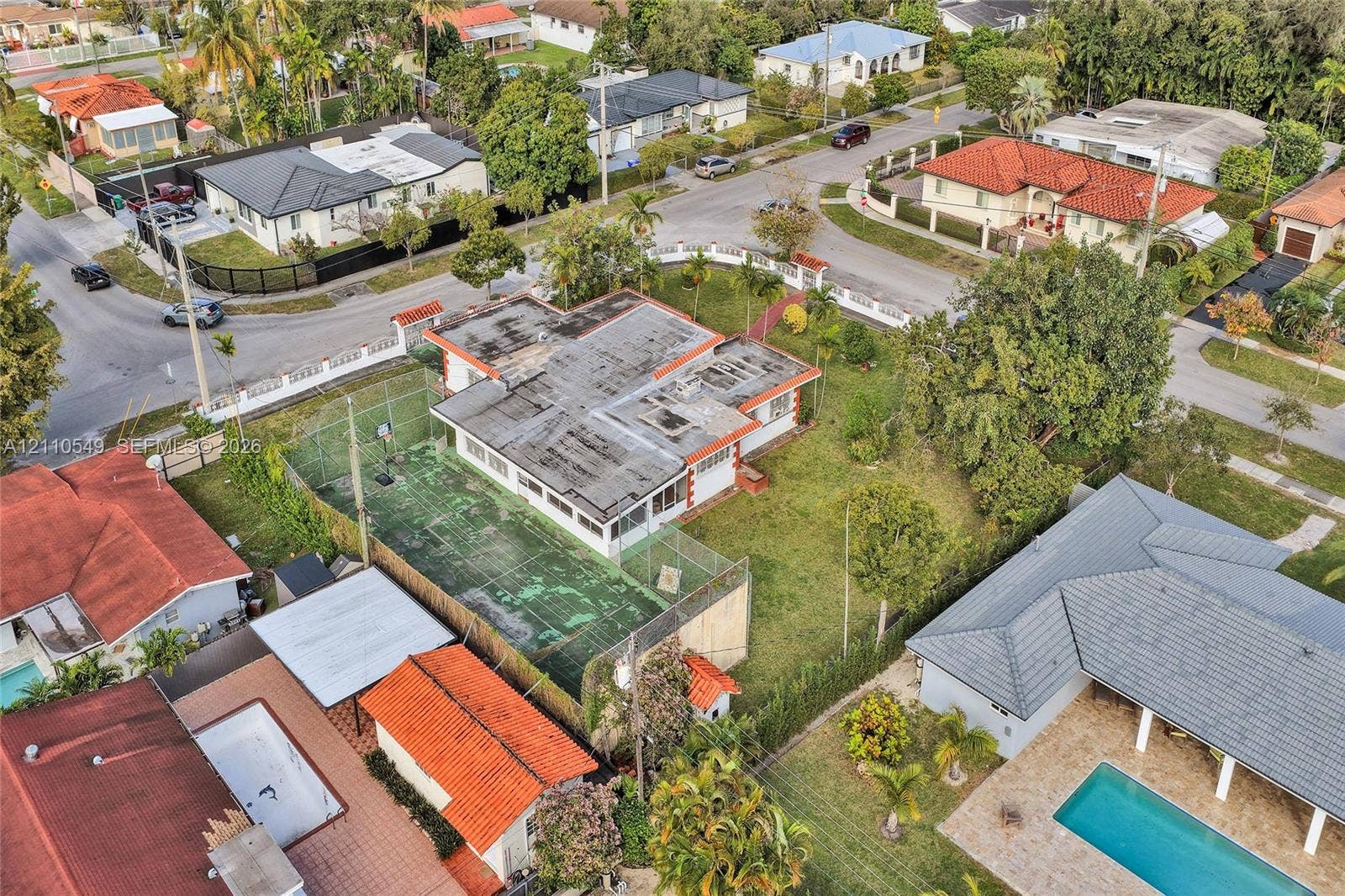500 SW 39th Court, Miami, FL 33134 Aerial perspective of a corner lot property featuring a private fenced sports court, expansive green space, and mature perimeter trees