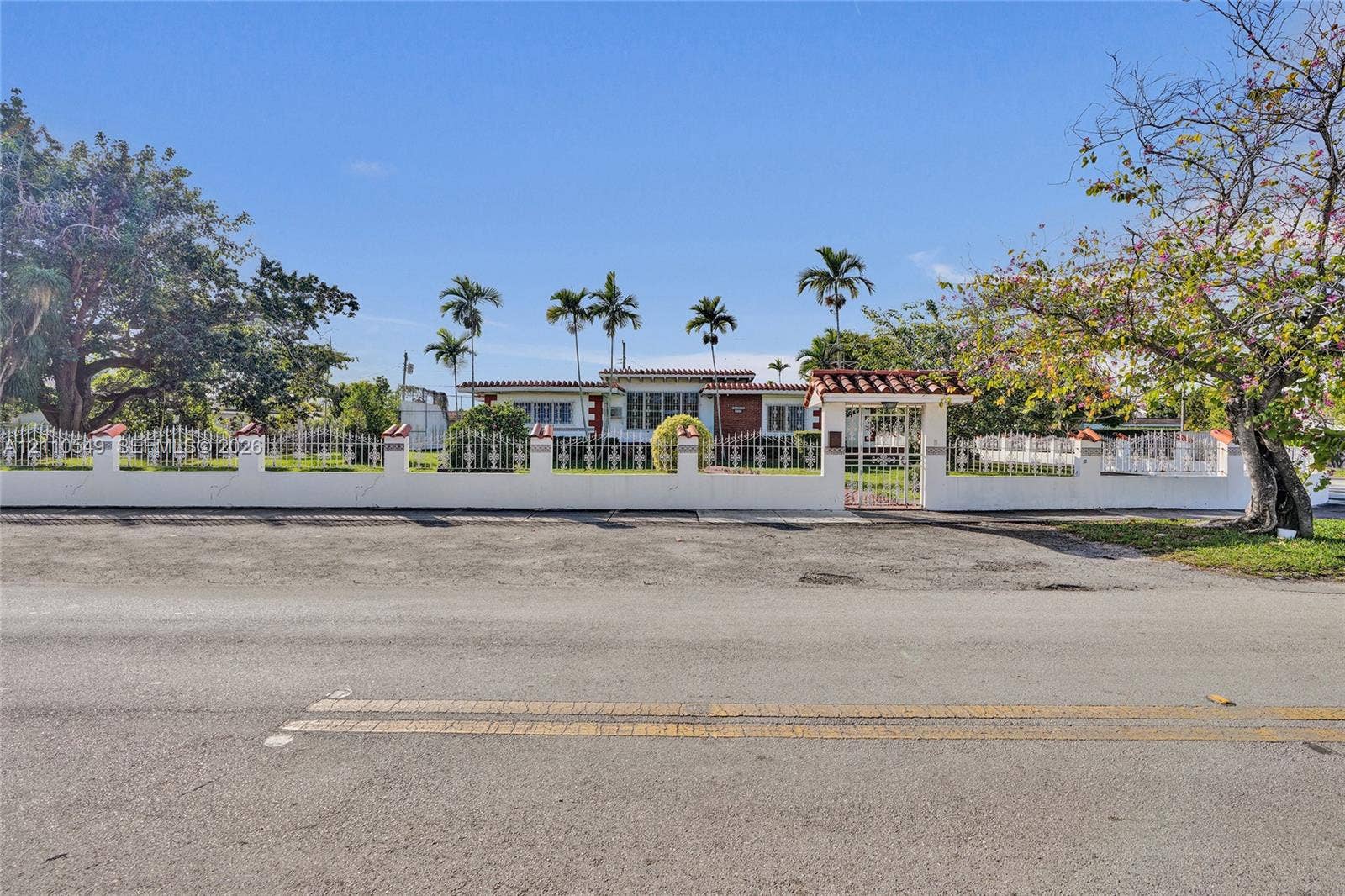 500 SW 39th Court, Miami, FL 33134 Single-story residence featuring a terracotta-tiled roof, white exterior masonry walls, a decorative metal perimeter fence, and a gated entrance