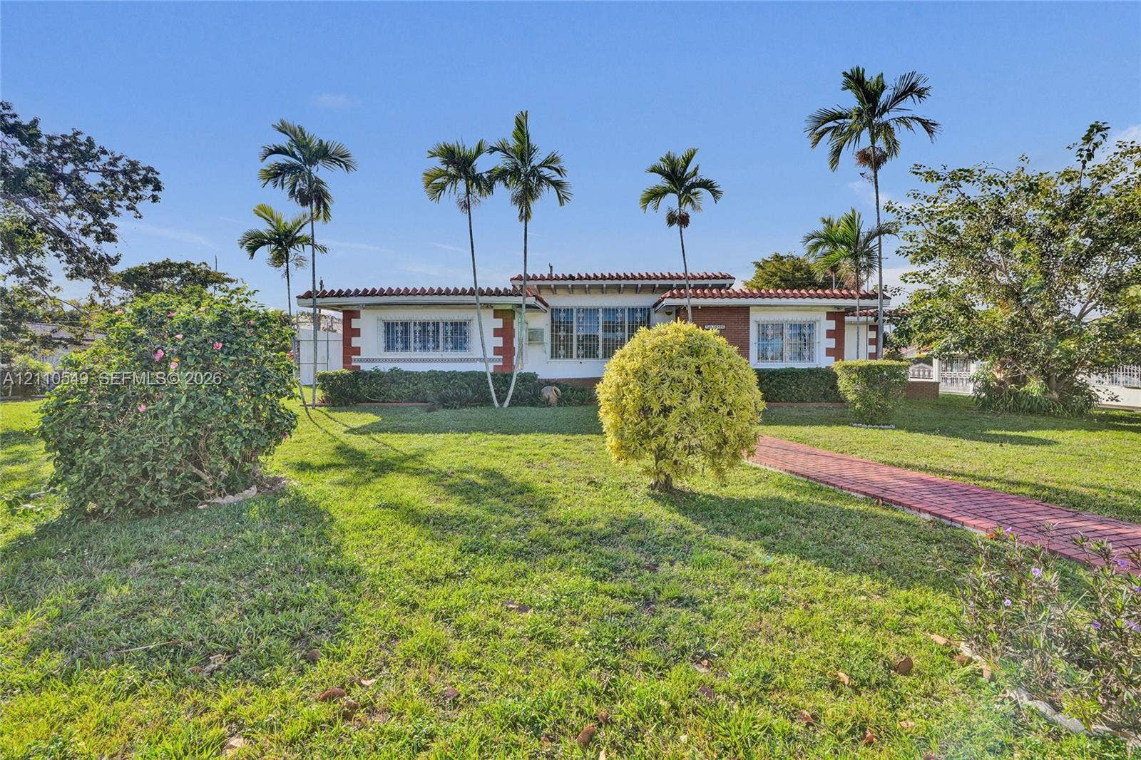 500 SW 39th Court, Miami, FL 33134 Single-story exterior featuring a clay tile roof, brick accents, multi-pane windows, and a paved brick walkway set within a landscaped lawn with mature palm trees