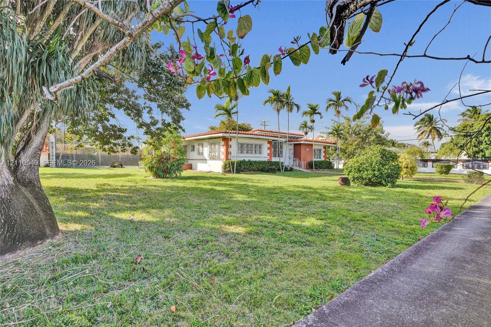 500 SW 39th Court, Miami, FL 33134 Single-story residence featuring a terracotta tile roof, masonry exterior, expansive grass lawn, and mature palm trees