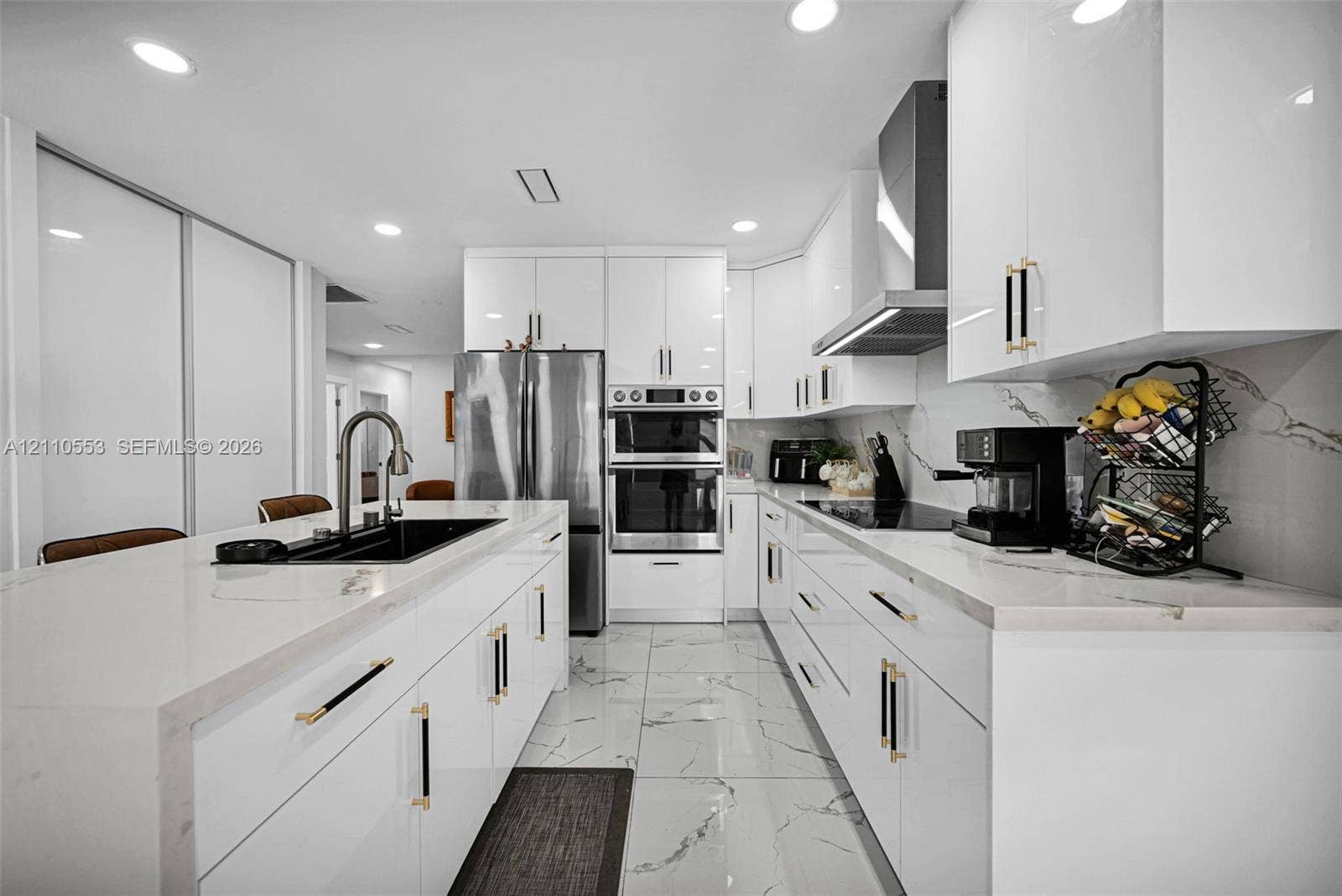 16611 SW 108th Court, Miami, FL 33157 Modern kitchen featuring high-gloss white cabinetry, white stone-finish countertops, large-format veined tile flooring, built-in double wall ovens, and a center island with a matte black undermount sink