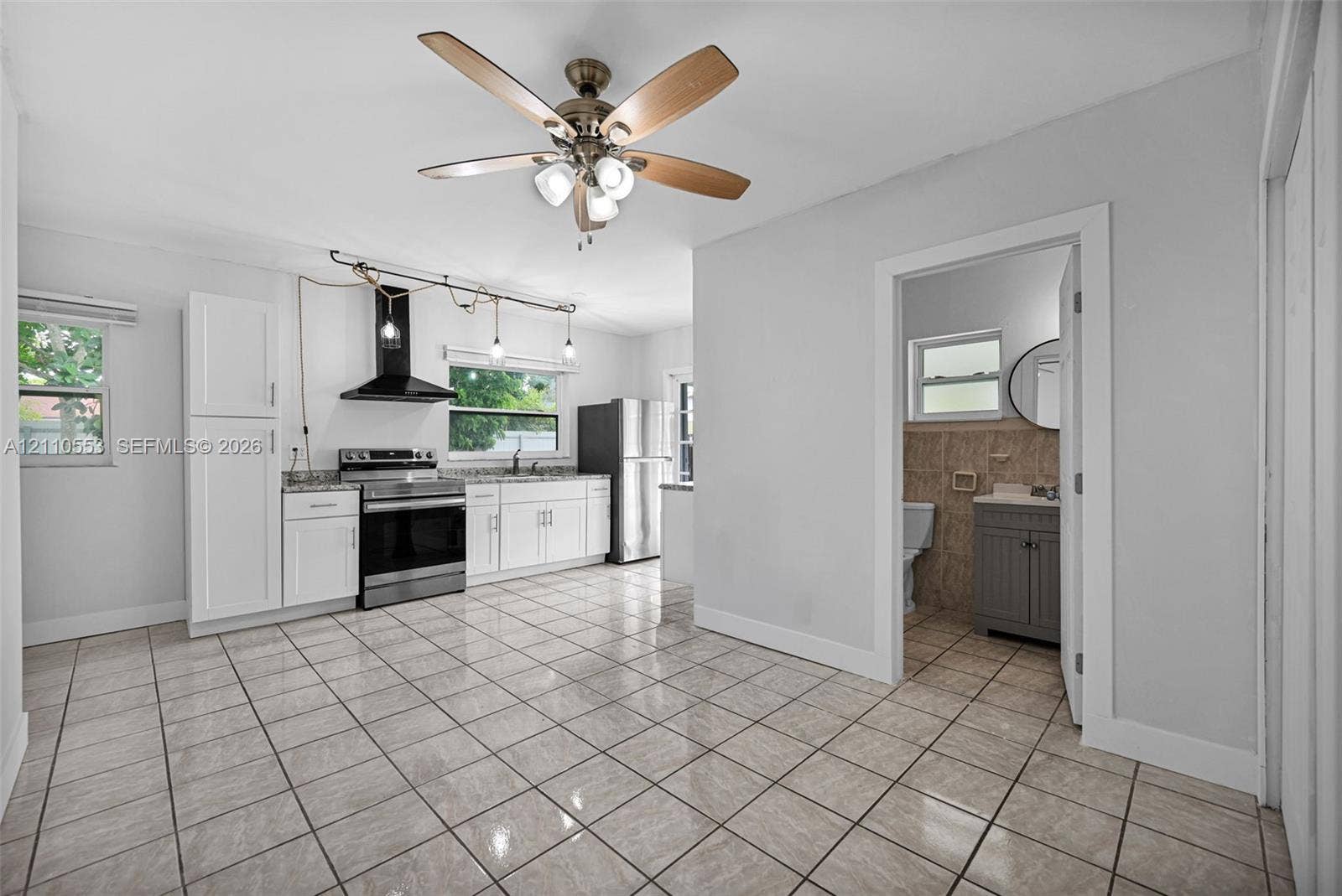 16611 SW 108th Court, Miami, FL 33157 Kitchen featuring white cabinetry, stainless steel appliances, a black range hood, tile flooring, and a ceiling fan with integrated lighting