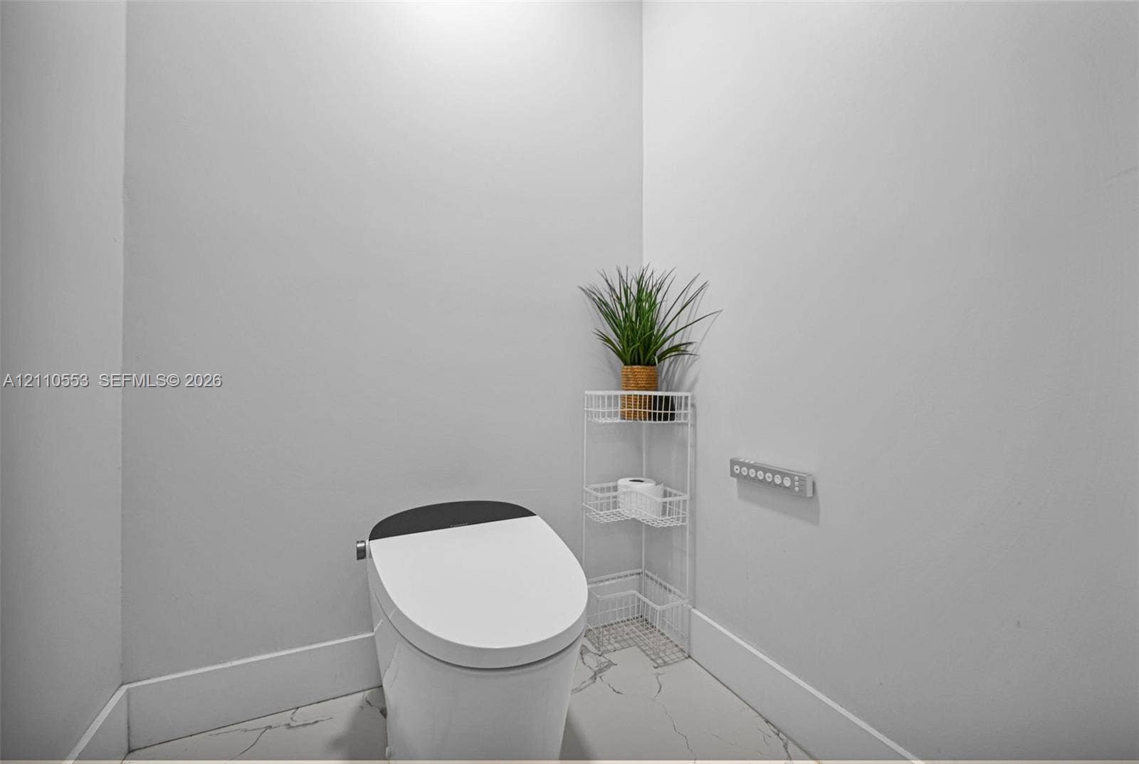 16611 SW 108th Court, Miami, FL 33157 Modern one-piece smart toilet featuring a streamlined profile and contrast lid, set against large-format tile flooring with marble-finish veining and wall-mounted digital control panel