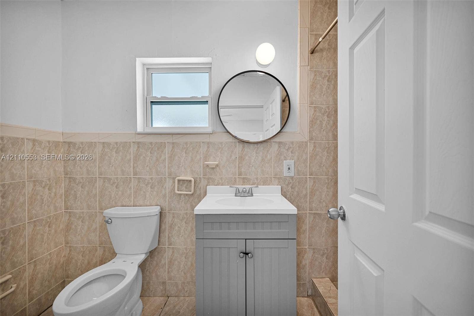 16611 SW 108th Court, Miami, FL 33157 Bathroom featuring neutral-toned wall tile, a gray vanity cabinet with a white countertop, a circular wall-mounted mirror, and a single-hung window