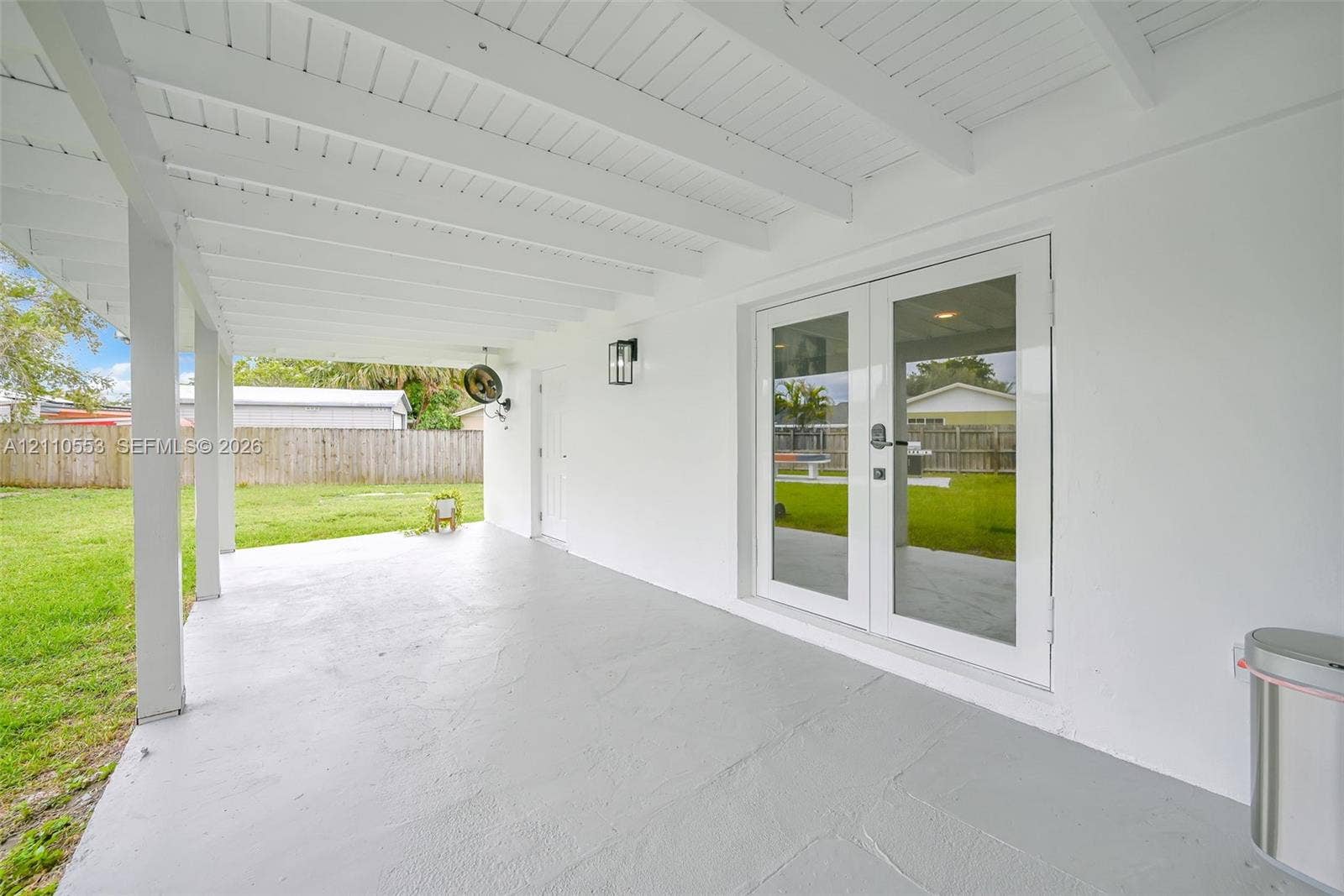 16611 SW 108th Court, Miami, FL 33157 Covered patio featuring a painted concrete floor, white-finished exposed beam ceiling, full-glass French doors, and wall-mounted exterior lighting