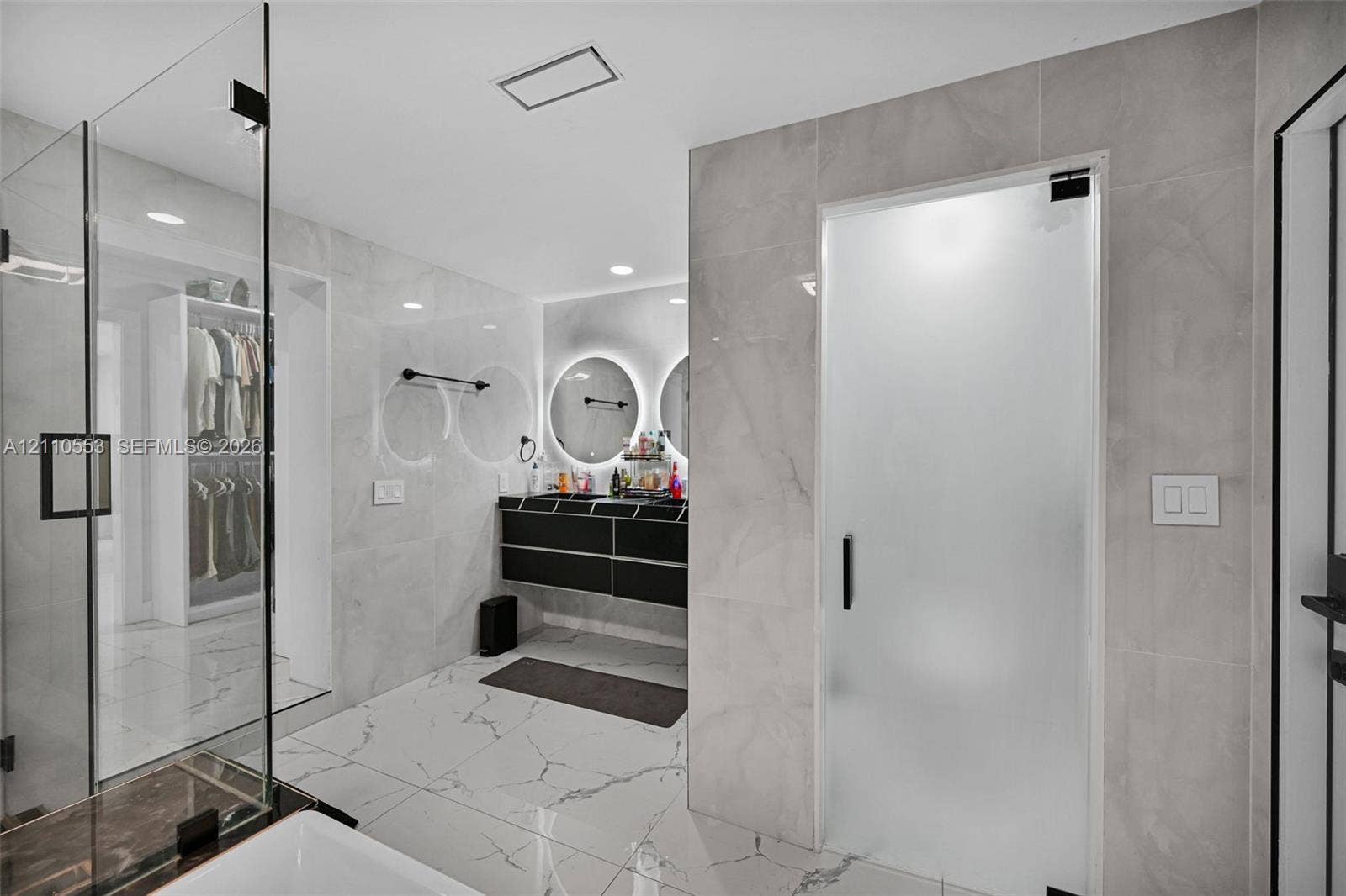 16611 SW 108th Court, Miami, FL 33157 Large-format tiled flooring, wall-to-wall stone-finish wall tiling, dual floating vanity with integrated lighting, glass-enclosed shower, and frosted glass privacy door