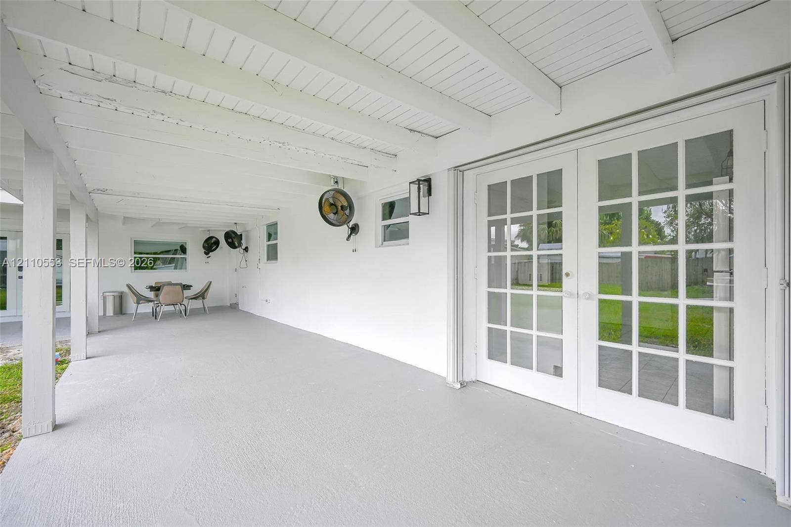 16611 SW 108th Court, Miami, FL 33157 Covered patio featuring a painted wood-beam ceiling, glass-paned French doors, exterior wall-mounted lighting, and concrete flooring