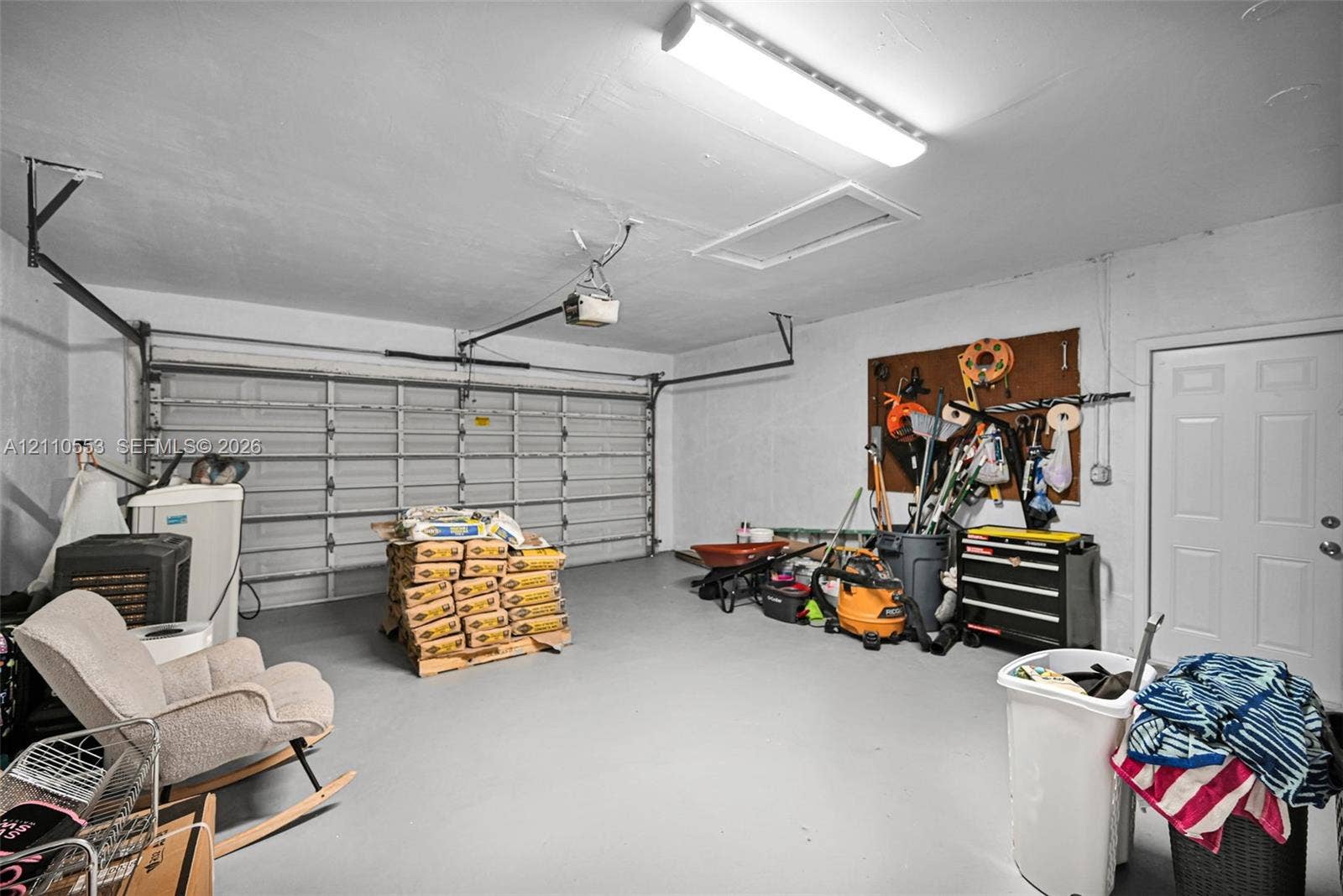 16611 SW 108th Court, Miami, FL 33157 Two-car garage featuring a sectional metal door, ceiling-mounted light fixture, attic access panel, and a pedestrian service door