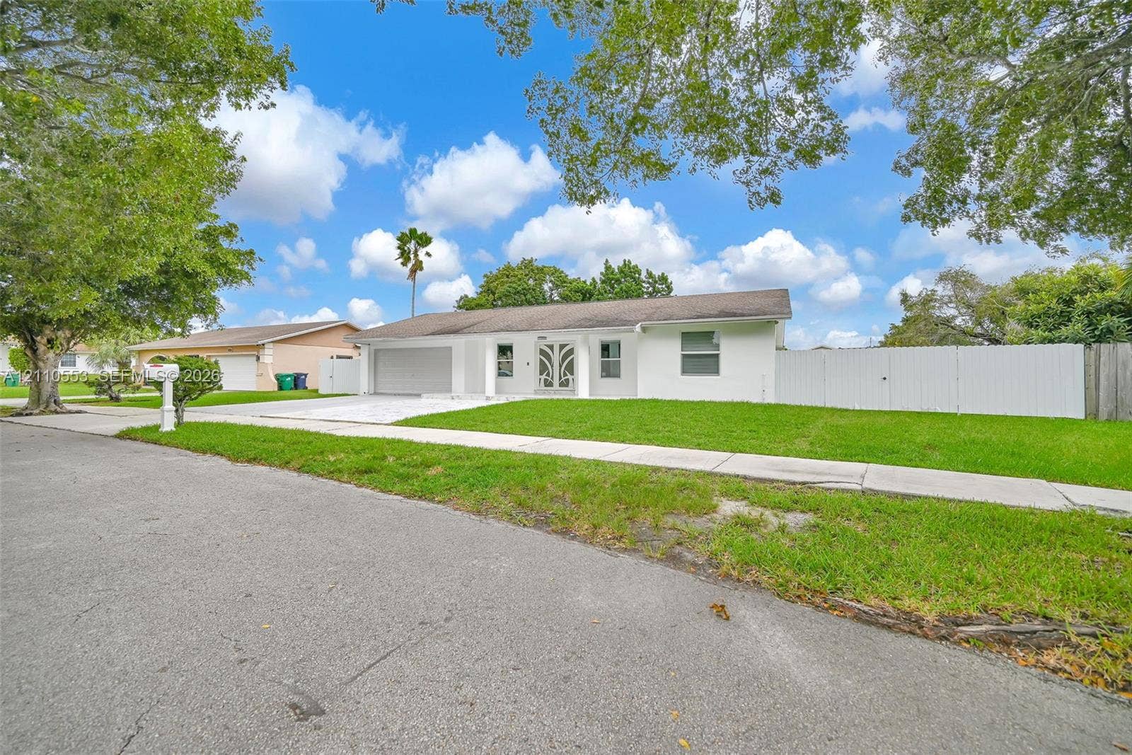 16611 SW 108th Court, Miami, FL 33157 Single-story exterior featuring a painted masonry facade, ornamental glass-paneled entry door, attached two-car garage, and full-perimeter privacy fencing