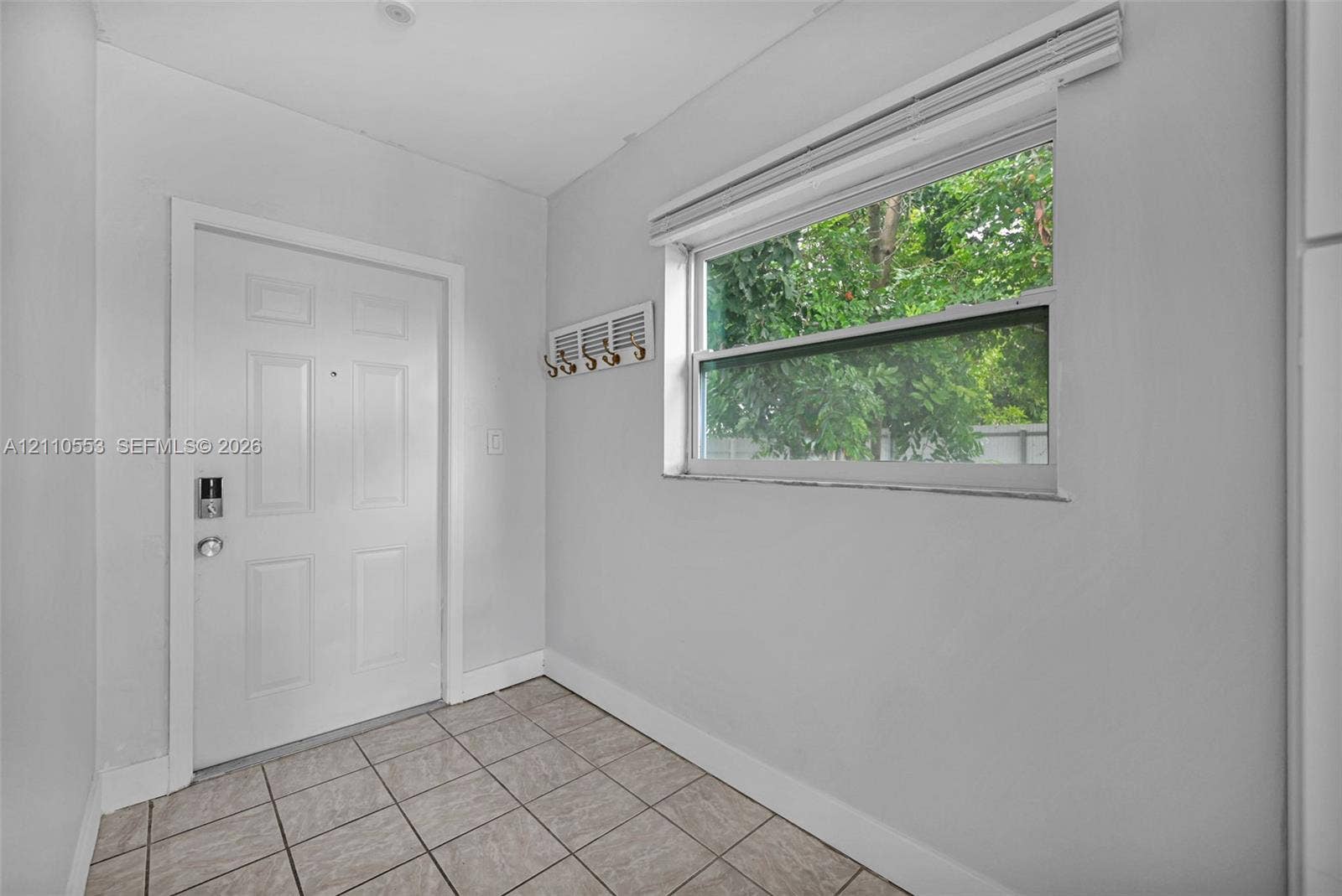 16611 SW 108th Court, Miami, FL 33157 Entry area featuring a solid-core door with electronic deadbolt, ceramic tile flooring, and a single-hung window with horizontal blinds