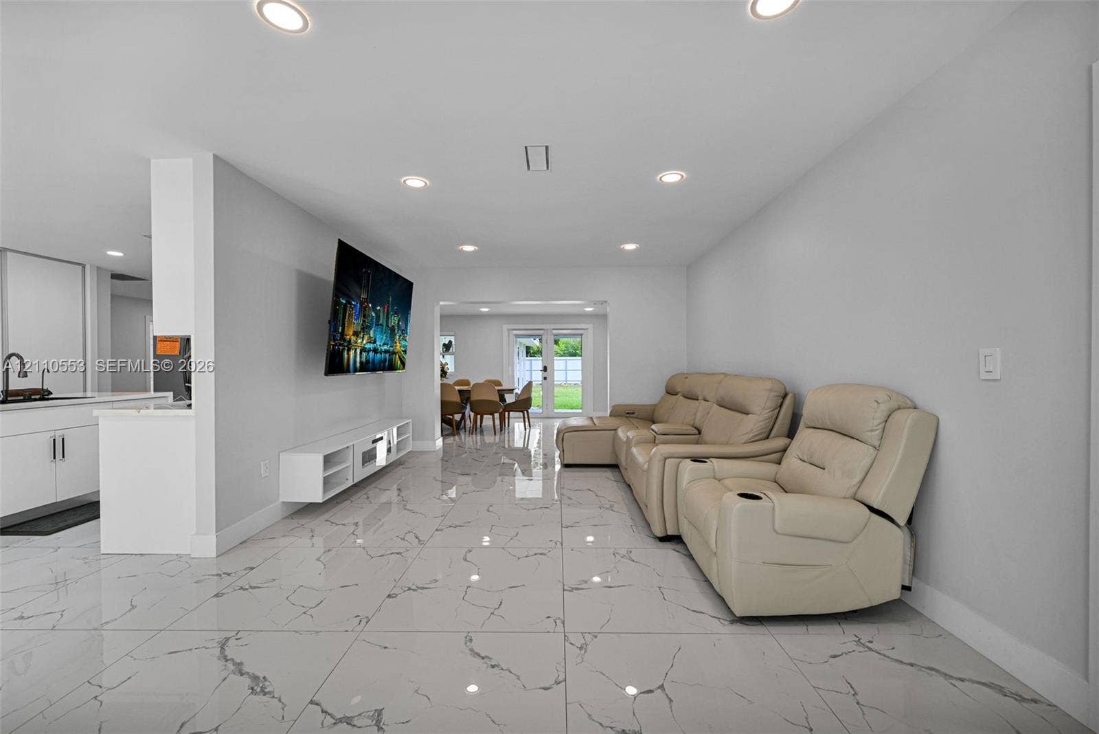 16611 SW 108th Court, Miami, FL 33157 Open-concept interior featuring large-format stone-patterned tile flooring, recessed ceiling lighting, a wall-mounted media console, and dual-pane glass entry doors