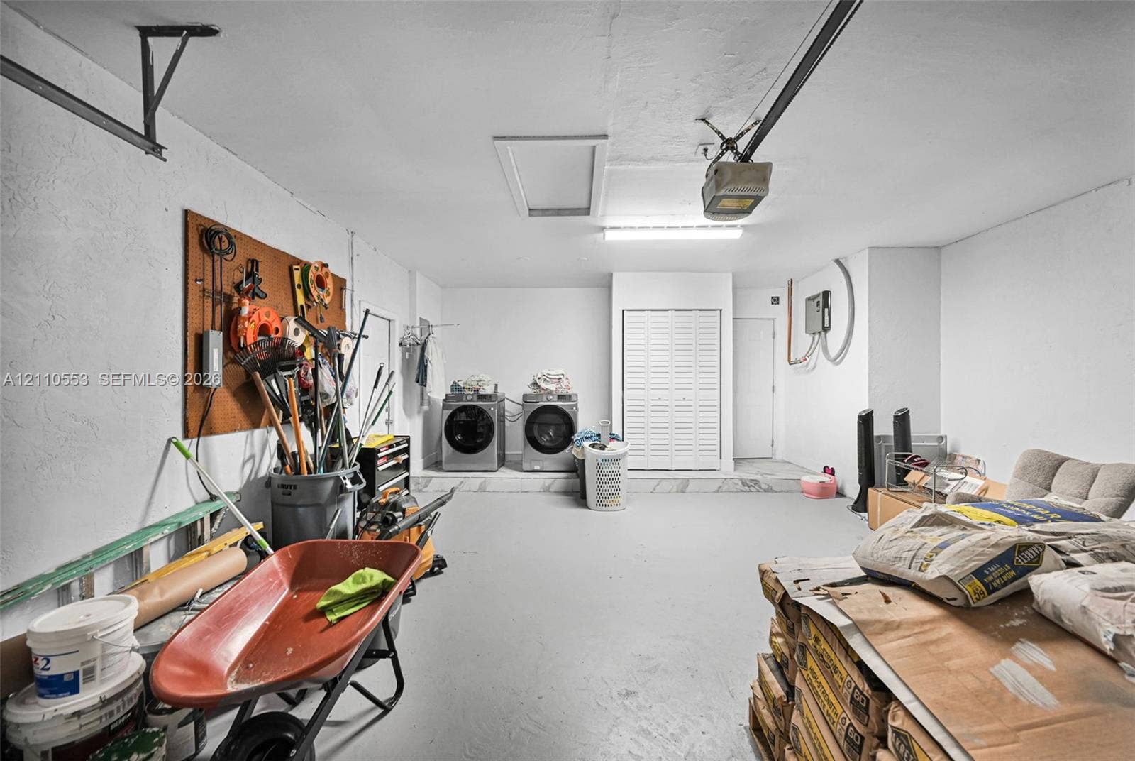 16611 SW 108th Court, Miami, FL 33157 Attached garage featuring a concrete floor, built-in wall storage board, overhead fluorescent lighting, and an integrated laundry area with louvered closet doors