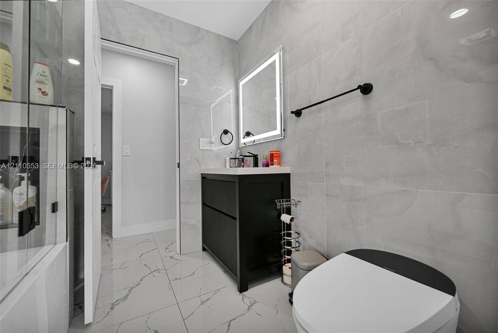 16611 SW 108th Court, Miami, FL 33157 Bathroom featuring large-format porcelain tile wall cladding, a black floating vanity with a solid surface countertop, an LED-backlit mirror, and matte black hardware