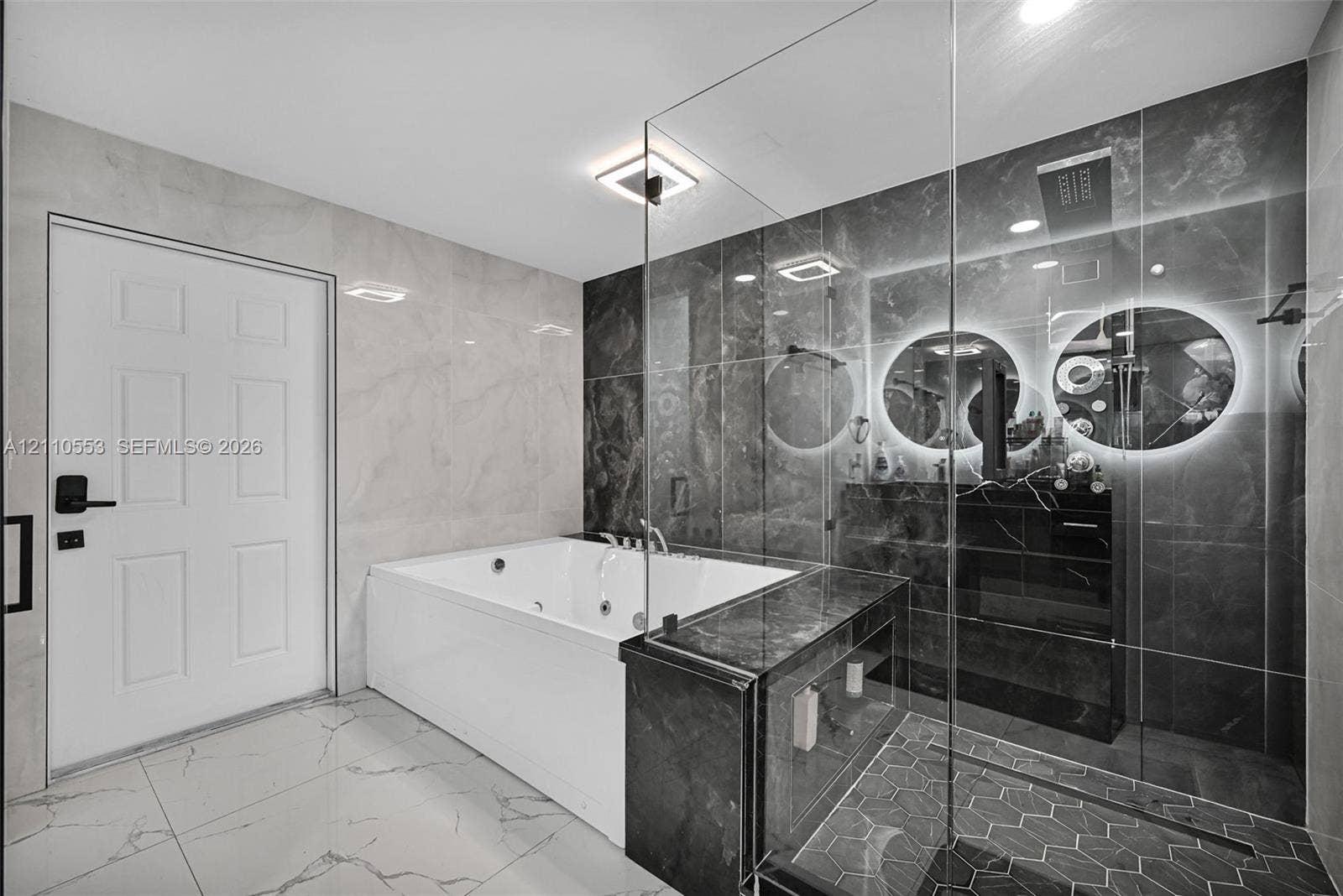 16611 SW 108th Court, Miami, FL 33157 Jetted soaking tub, walk-in shower with glass enclosure, large-format tile flooring, polished stone wall surfacing, and dual illuminated circular mirrors