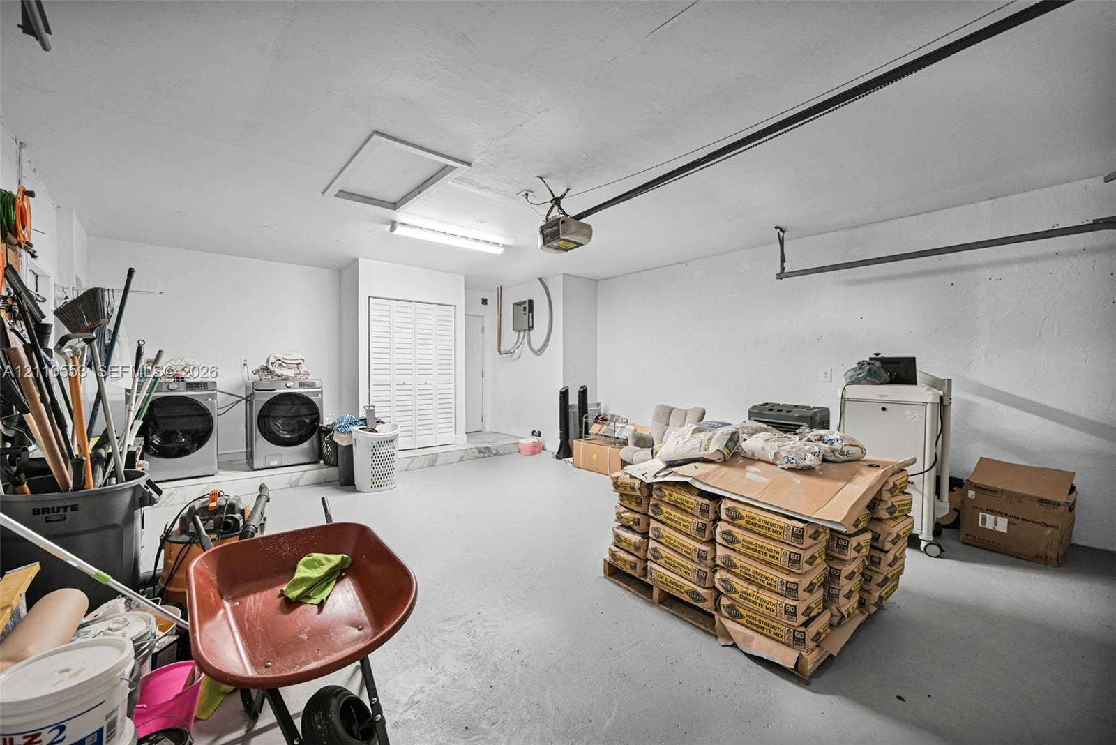 16611 SW 108th Court, Miami, FL 33157 Garage space featuring a painted concrete floor, ceiling-mounted garage door opener, overhead lighting, and dedicated laundry hookups with bifold closet doors