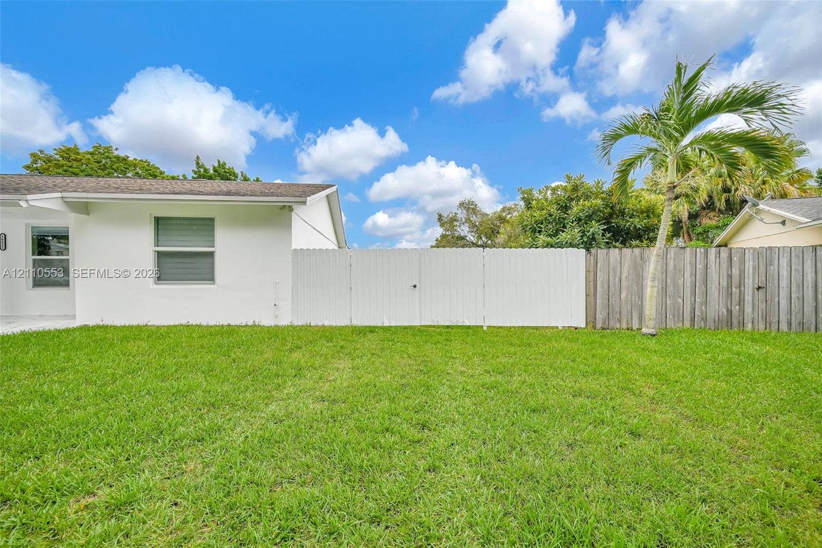 16611 SW 108th Court, Miami, FL 33157 Backyard featuring a manicured lawn, white vinyl privacy fencing, natural wood-finish fencing, and mature palm tree